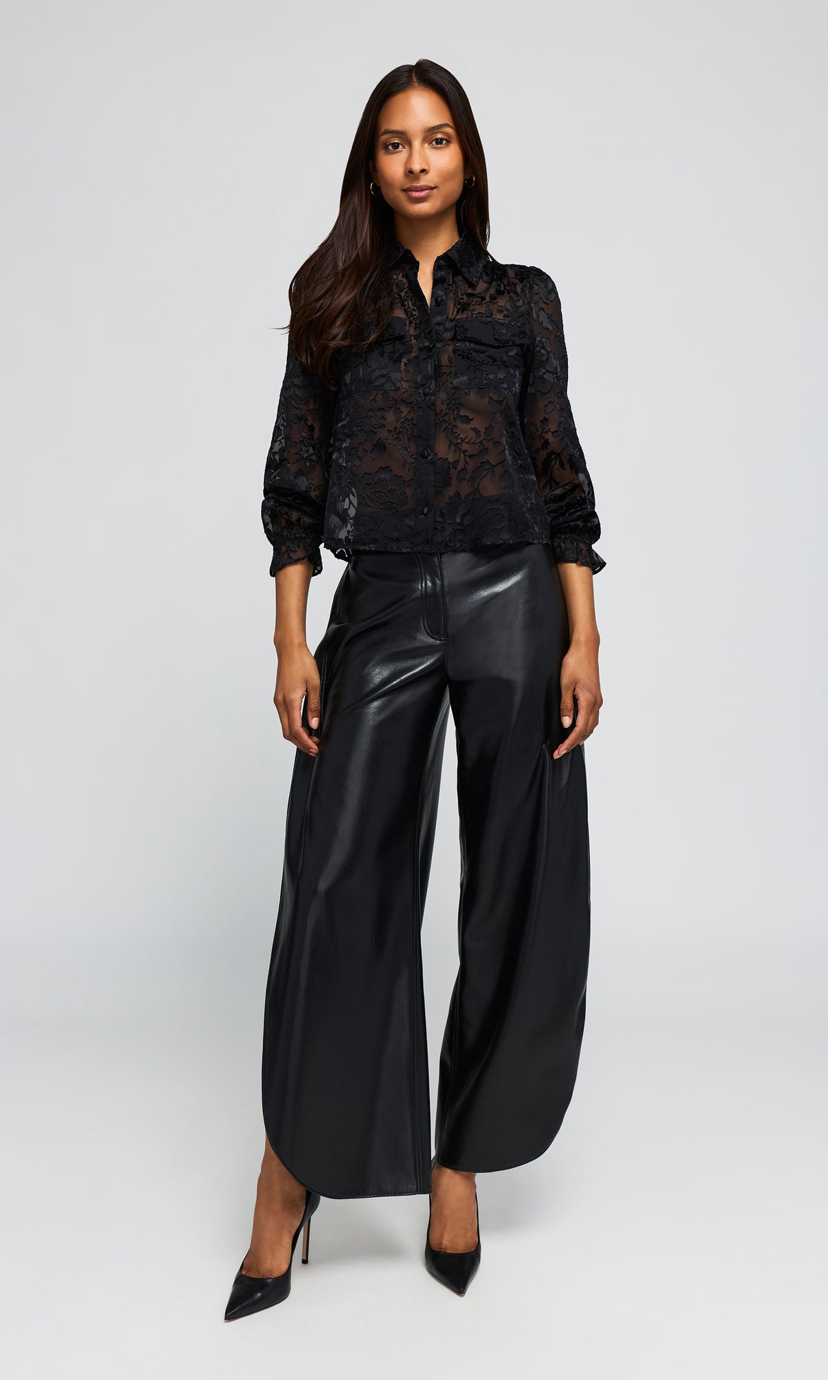Model wearing a black sheer lace long-sleeve blouse paired with black wide-leg faux-leather pants and black pointed-toe heels.