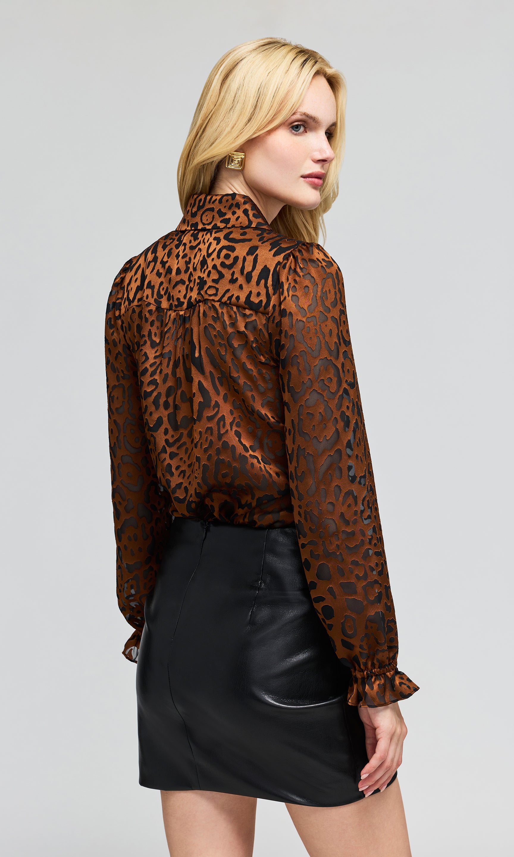 Back view of model wearing a brown and black leopard-print long-sleeve blouse with a black faux-leather wrap mini skirt.