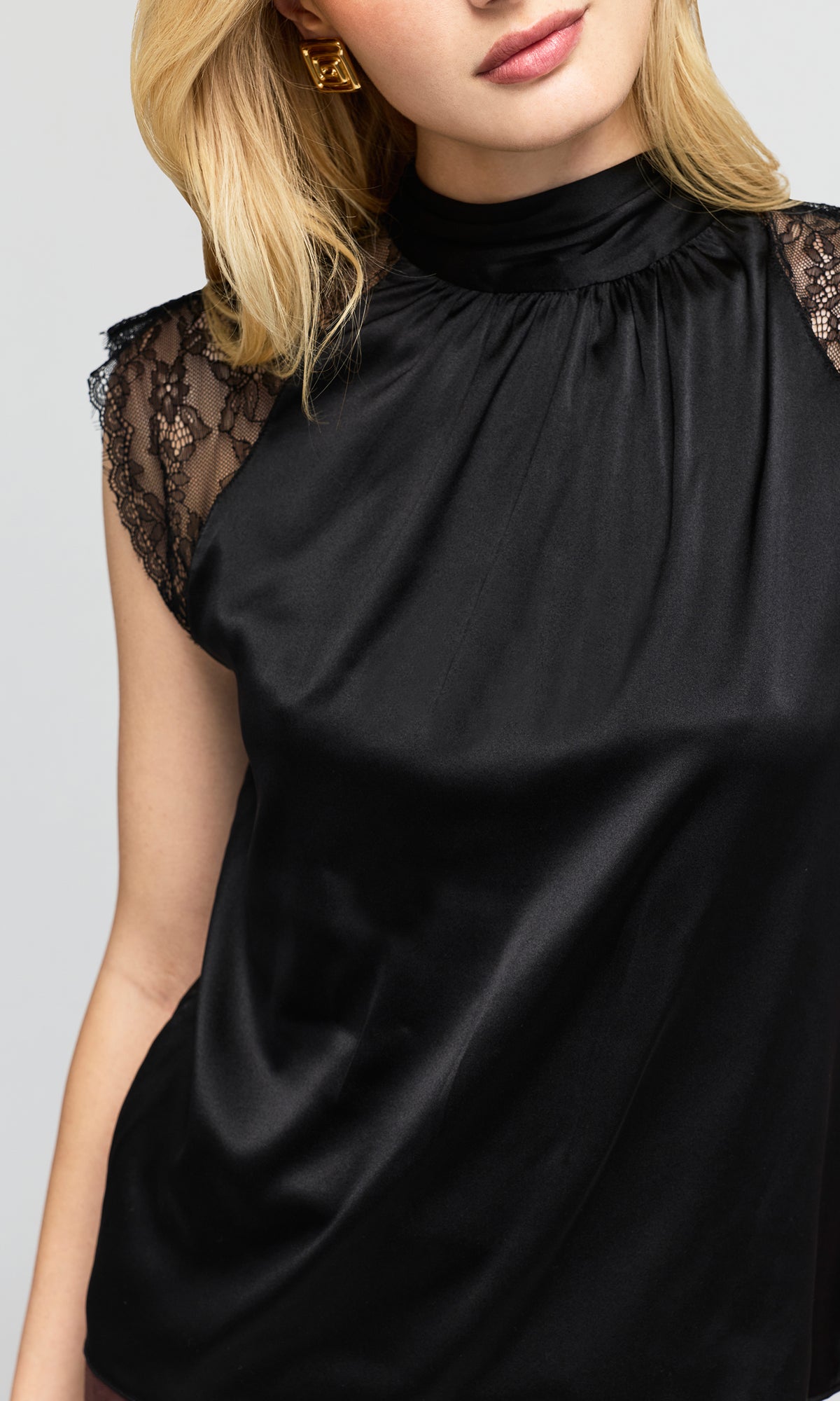 Close-up of a black satin mock-neck top with sheer black lace cap sleeves.