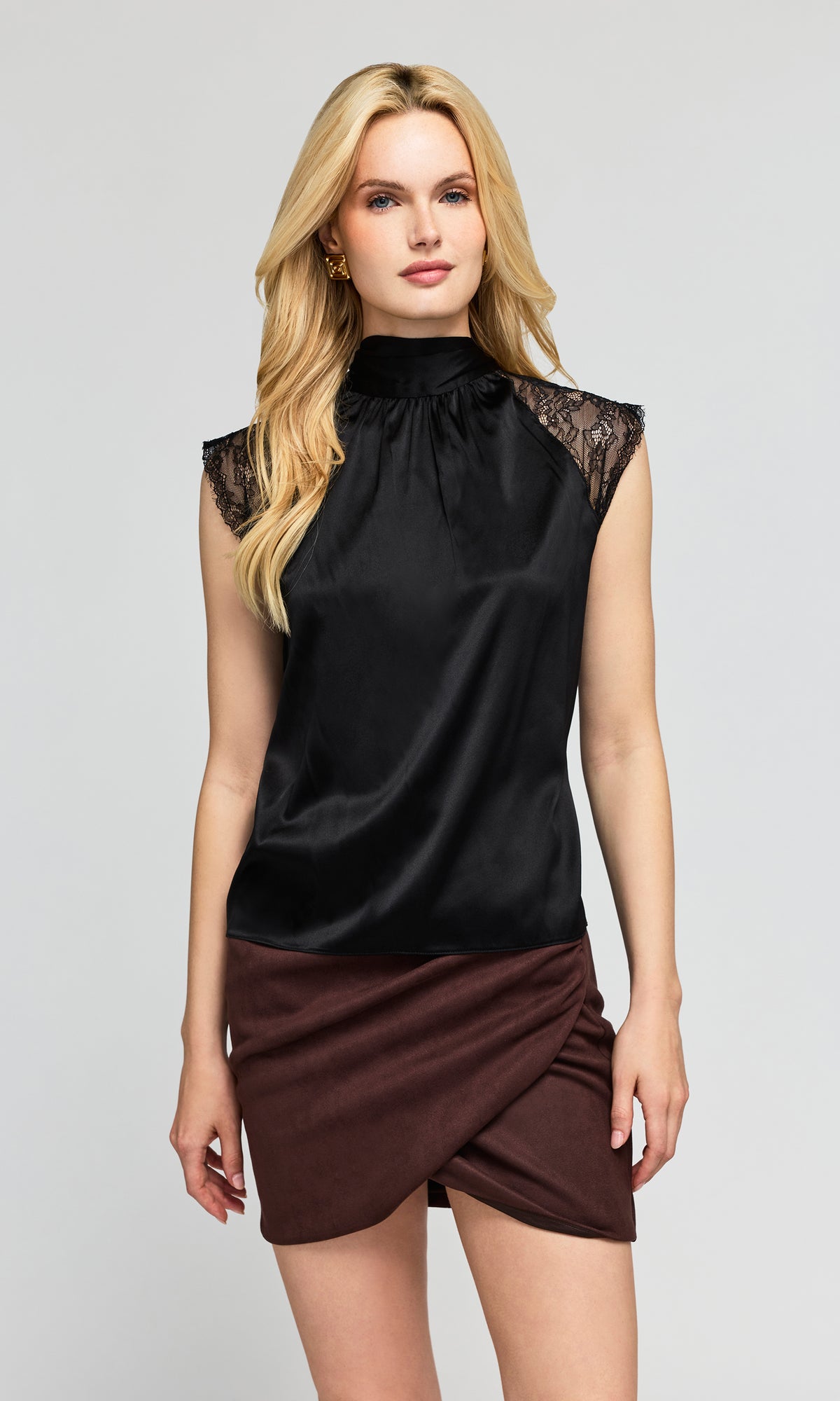 Model wearing a black satin sleeveless mock-neck top with lace cap sleeves and a dark brown wrap-style mini skirt.