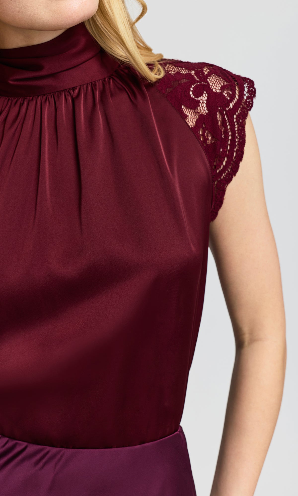 Close-up of a woman wearing a sleeveless high-neck top in deep burgundy satin with lace cap sleeves.