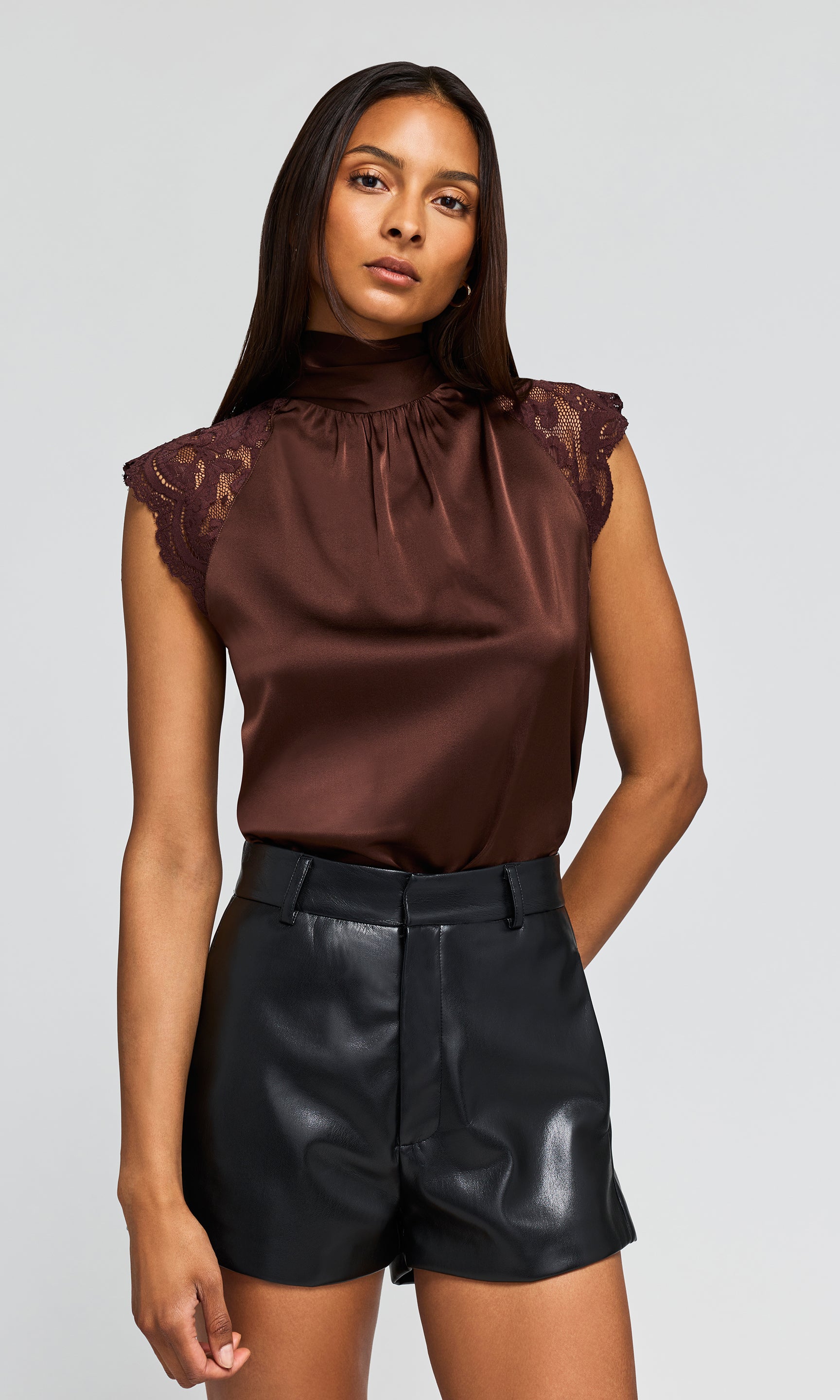 Model wearing a brown satin sleeveless blouse with lace cap sleeves and black faux-leather shorts .