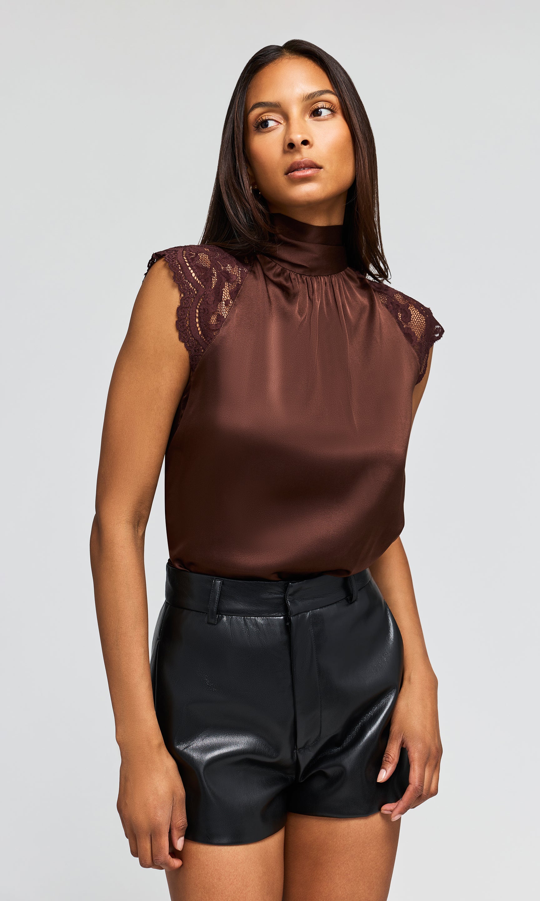 Side view of model wearing a brown satin sleeveless blouse with lace cap sleeves and black faux-leather shorts .