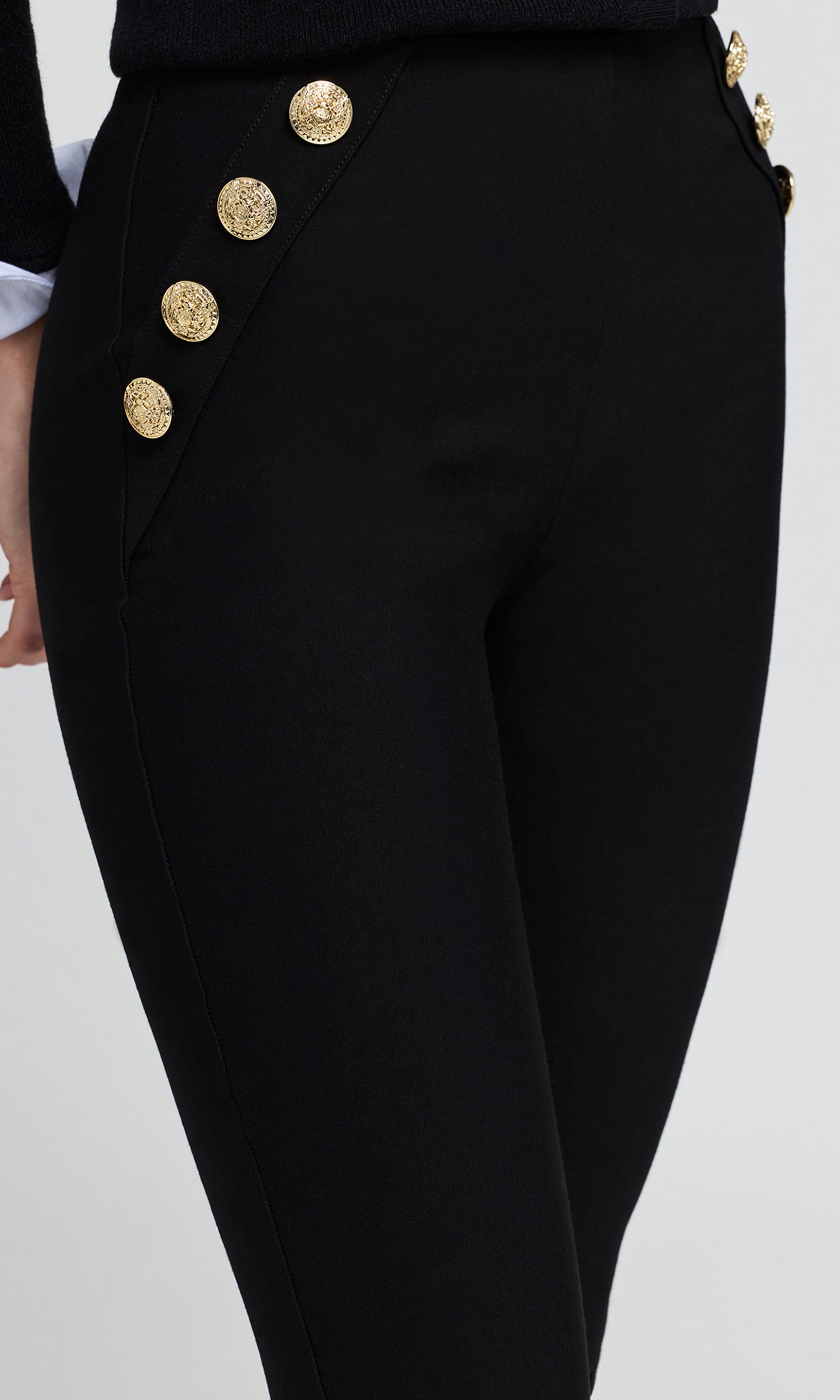 Close-up of black high-waisted trousers featuring a row of decorative gold buttons down the side.