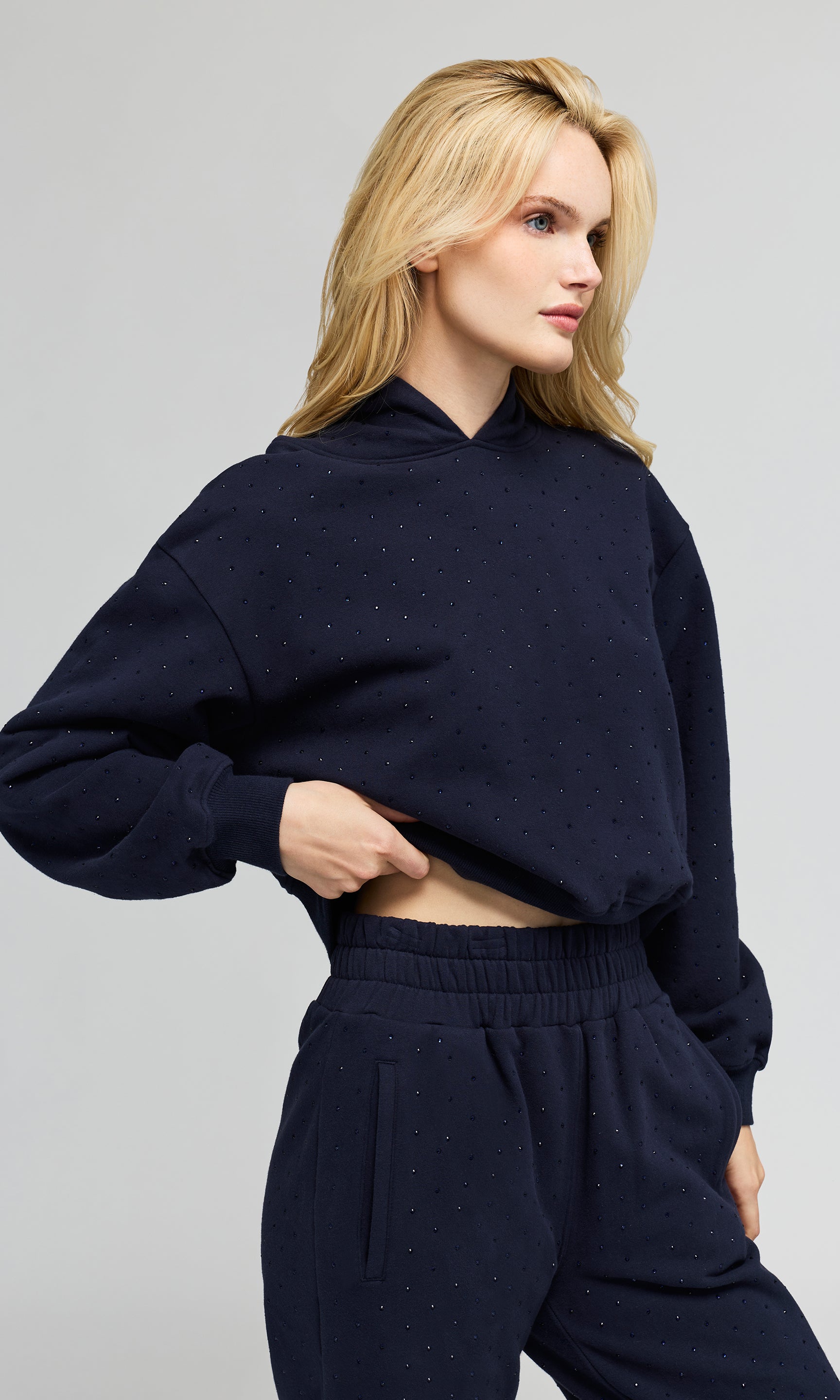 Side view of model wearing a navy hoodie sweatshirt and matching sweatpants, with crystal embellishments on a plain background.