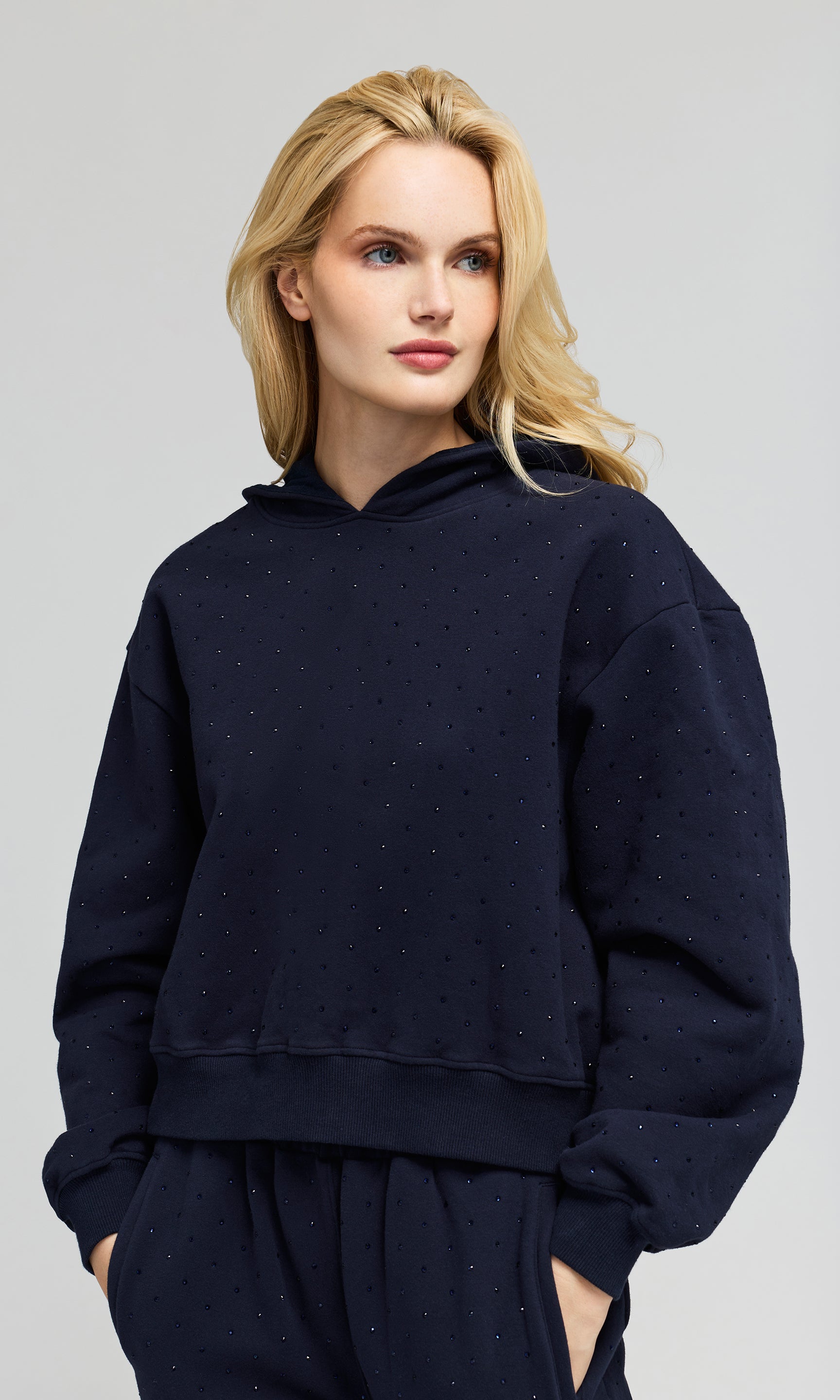 3/4 view of model wearing a navy hoodie sweatshirt and matching sweatpants, with crystal embellishments on a plain background.