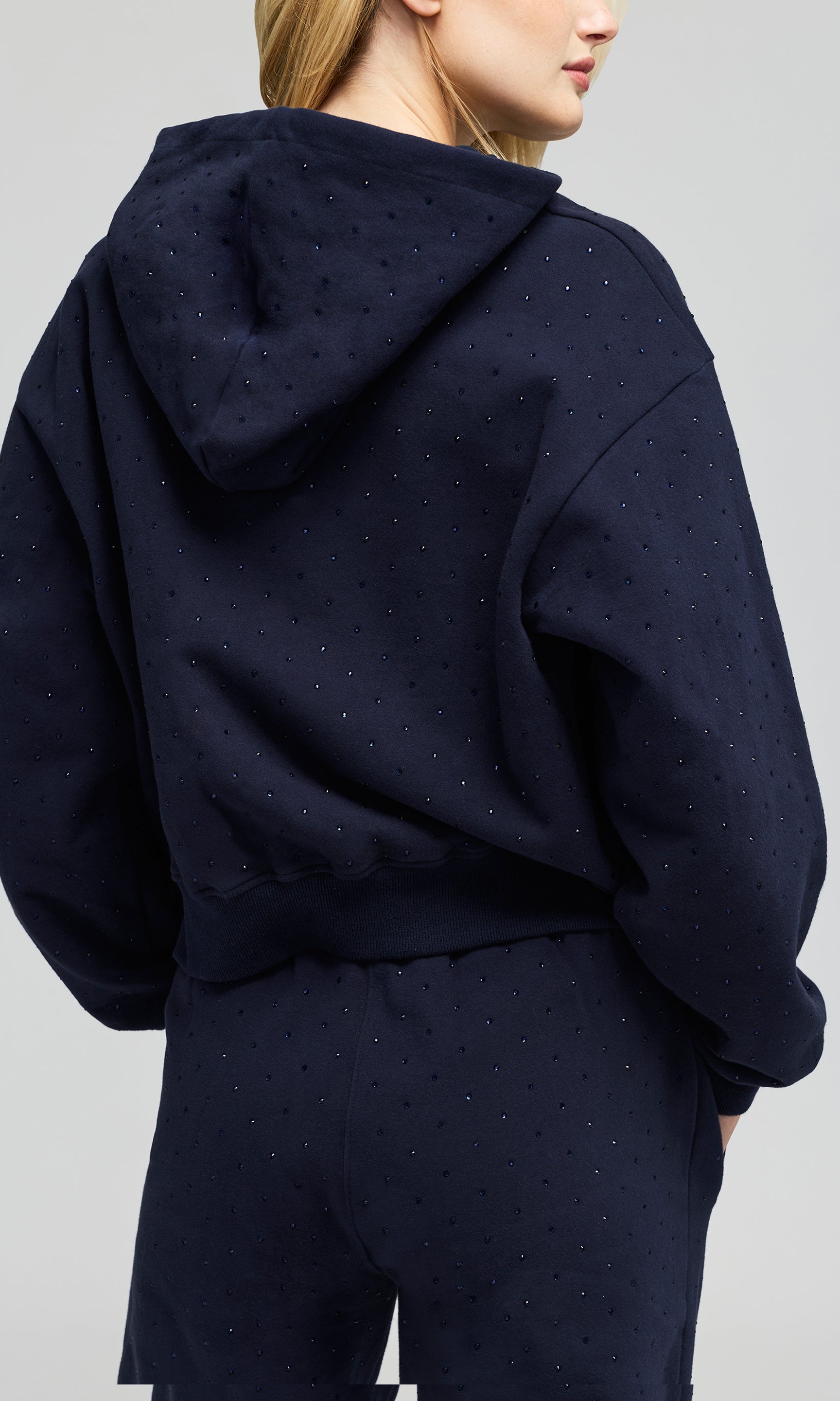 Back view of model wearing a navy hoodie sweatshirt and matching sweatpants, with crystal embellishments on a plain background.