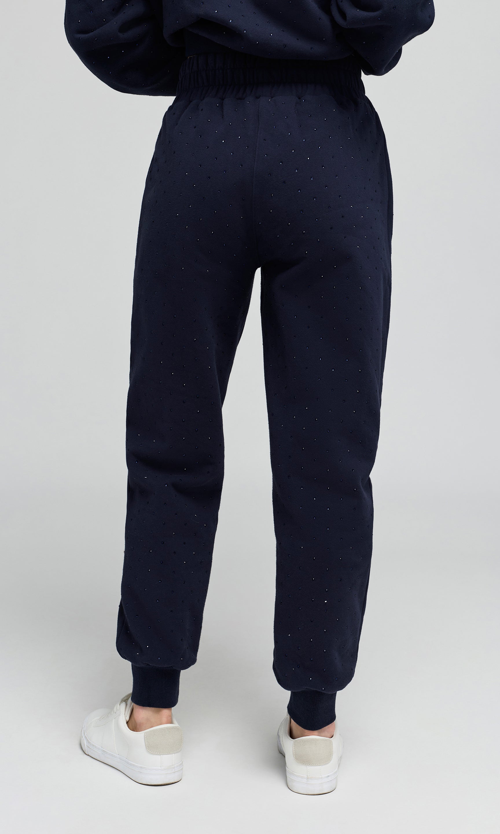 Back view of model wearing a navy jogger sweatpants with crystal embellishments on a plain background.