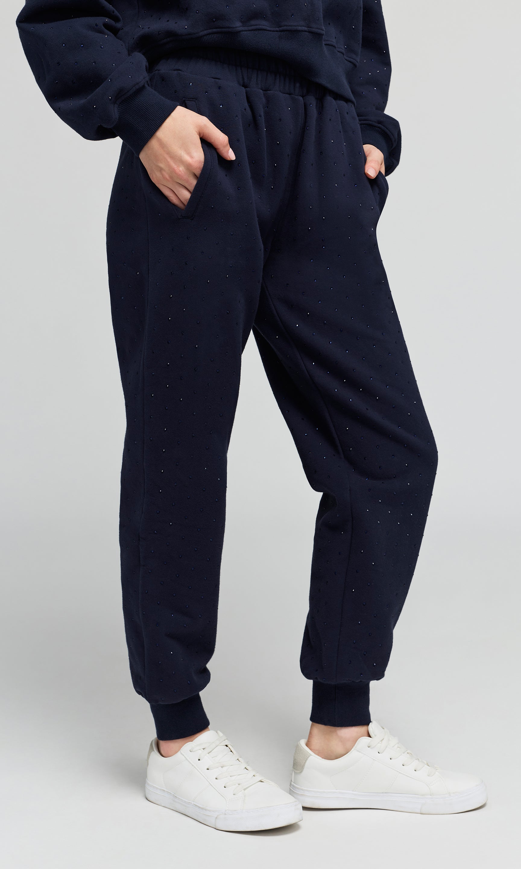 Side view of model wearing a navy jogger sweatpants with crystal embellishments on a plain background.