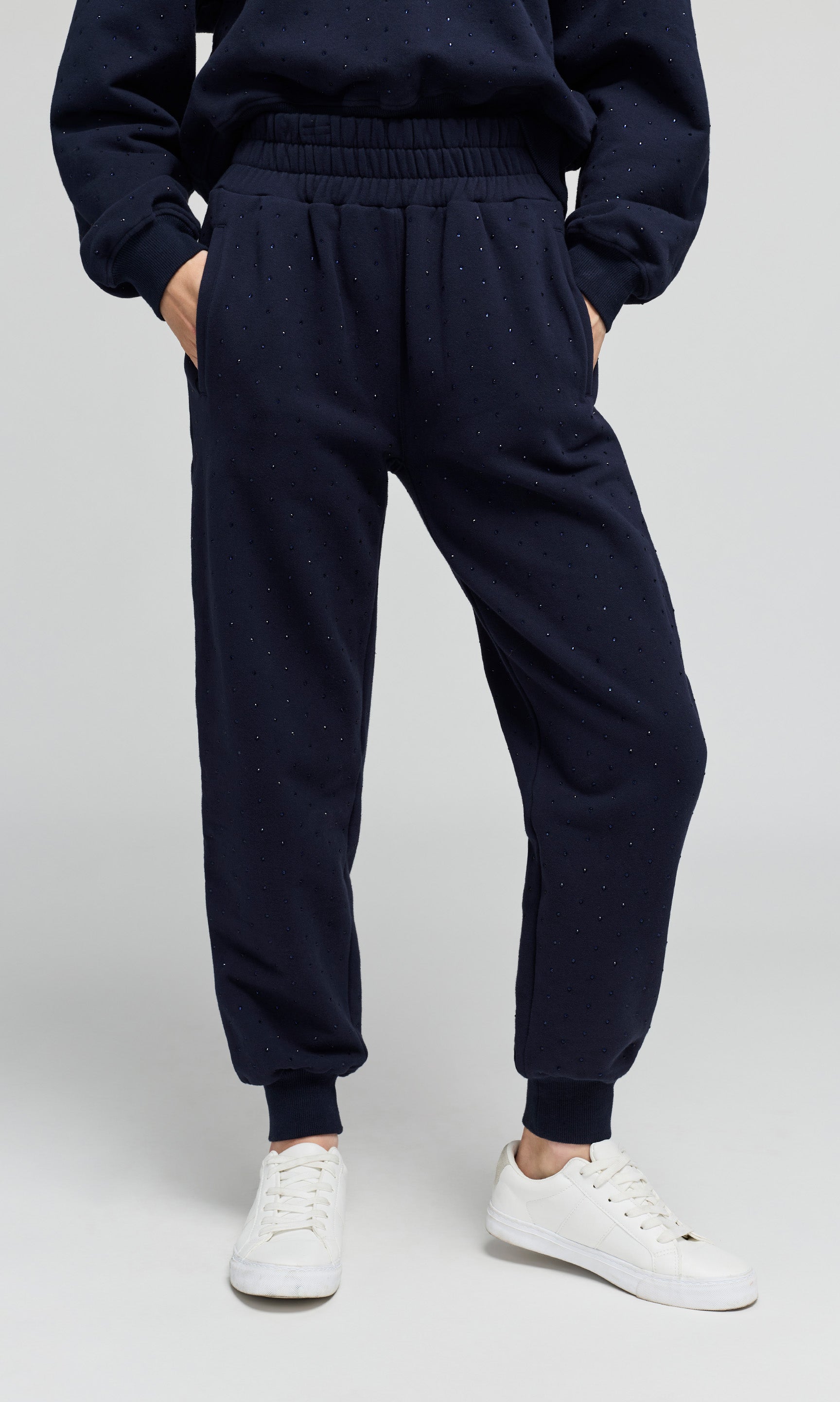 Model wearing a navy jogger sweatpants with crystal embellishments on a plain background.