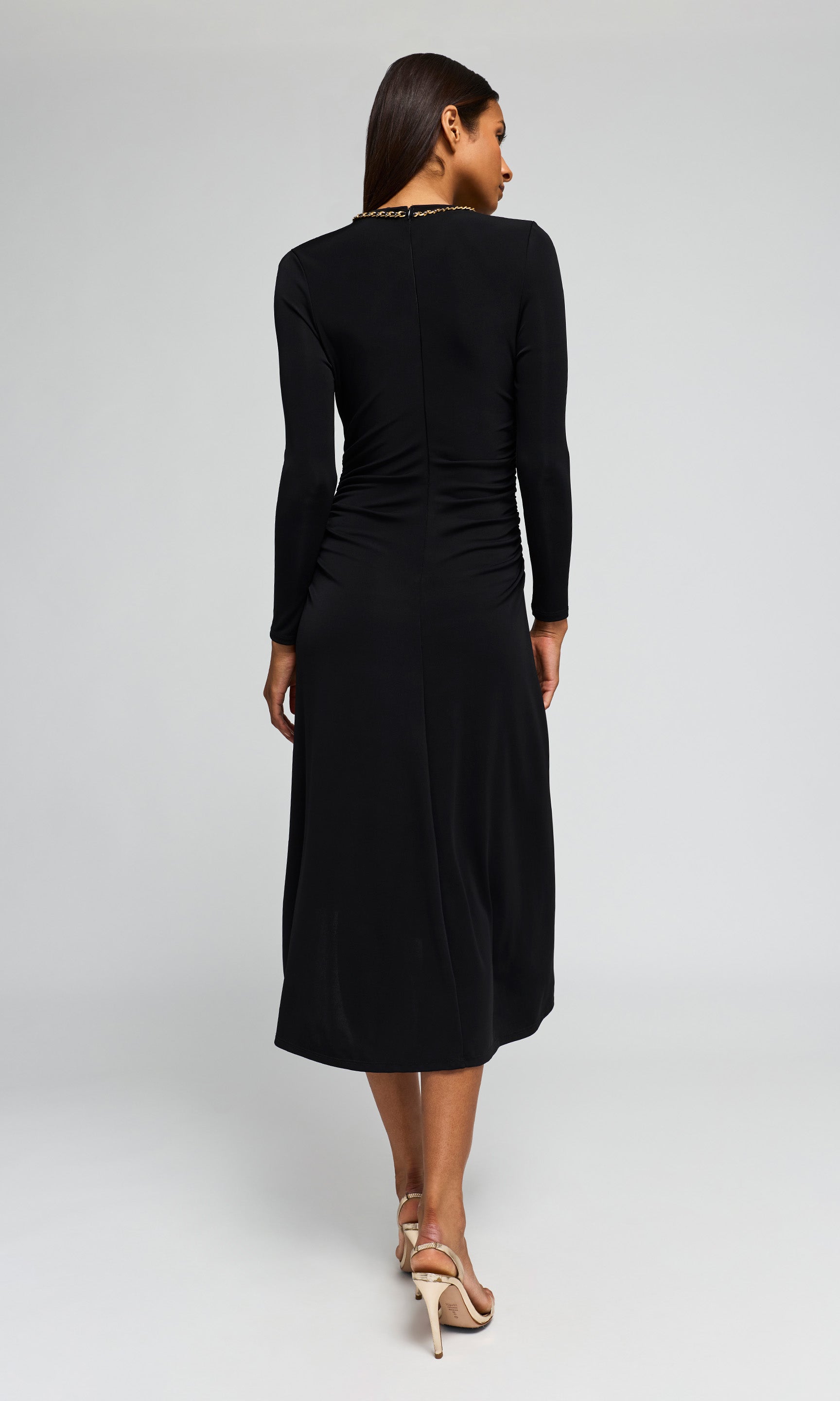 Back view of model wearing a black long-sleeve midi dress with a gathered, ruched bodice on a background.
