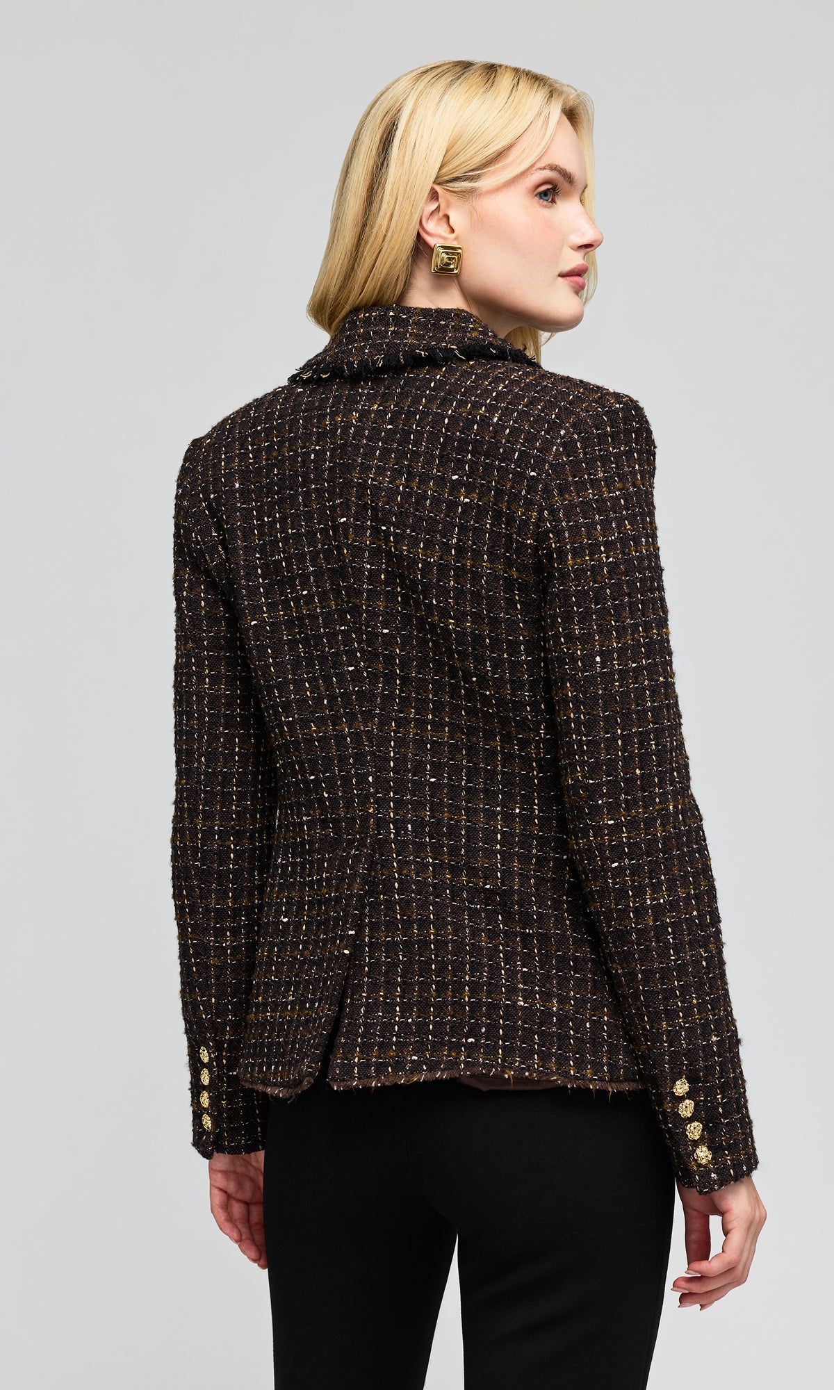 Back view of model wearing a dark tweed blazer with a subtle gold and beige check pattern, paired with black pants.