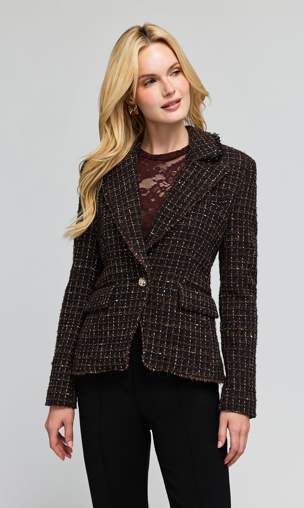 Model wearing a double breasted brown tweed blazer with gold button details over a burgundy top and black pants.