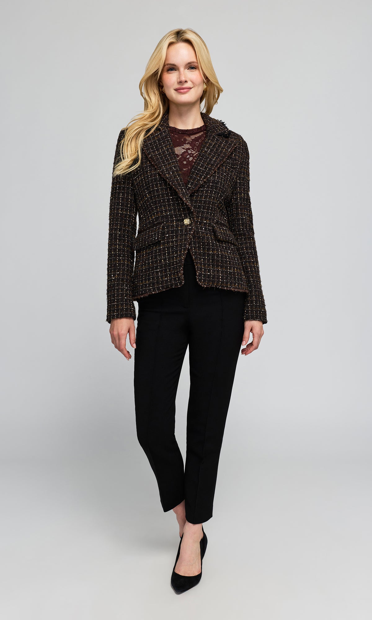 Model wearing a tailored blazer in a dark brown and black tweed pattern, paired with black trousers and black pointed-toe heels.