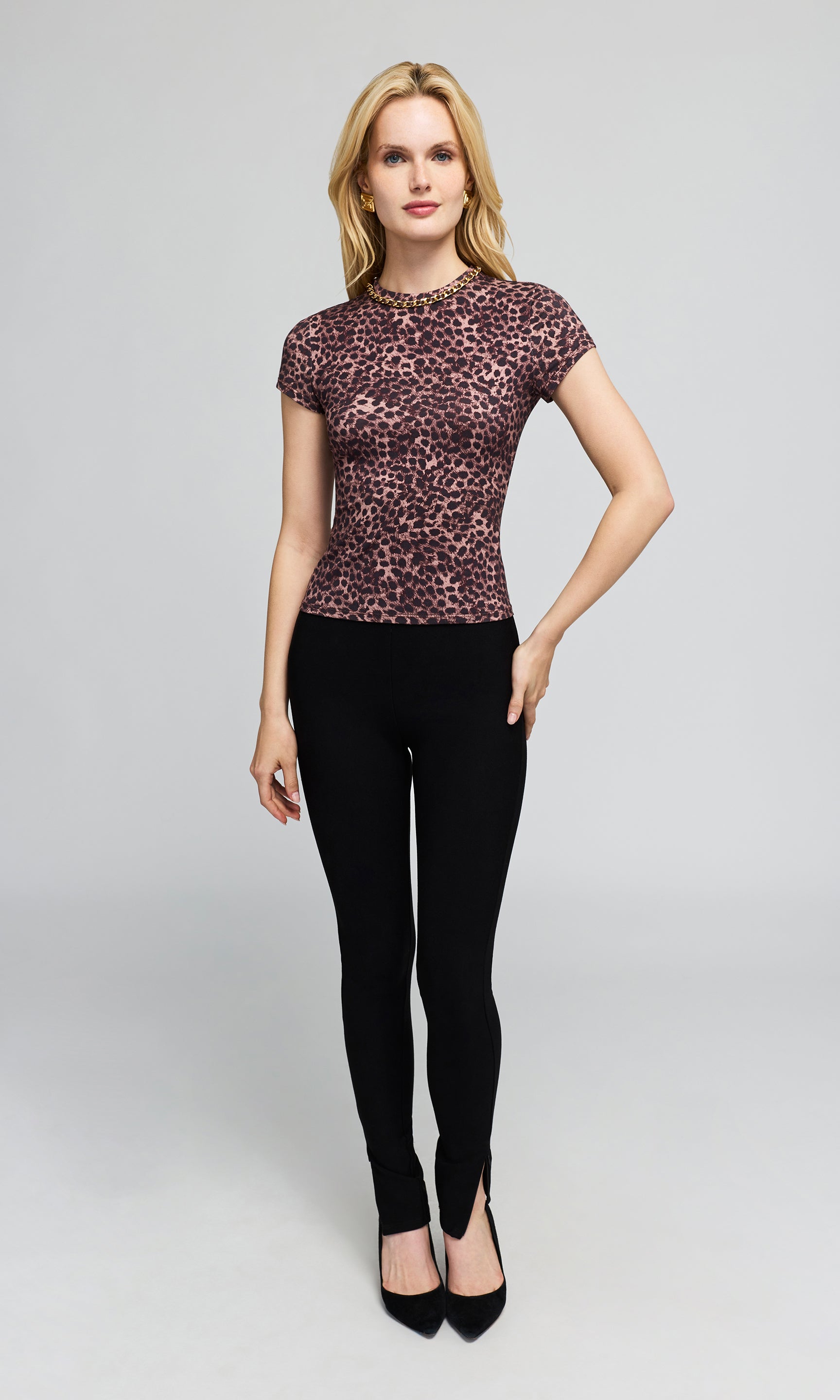 Model wearing a fitted short-sleeve top with a pink and black leopard print, black leggings, and black pointed heels.