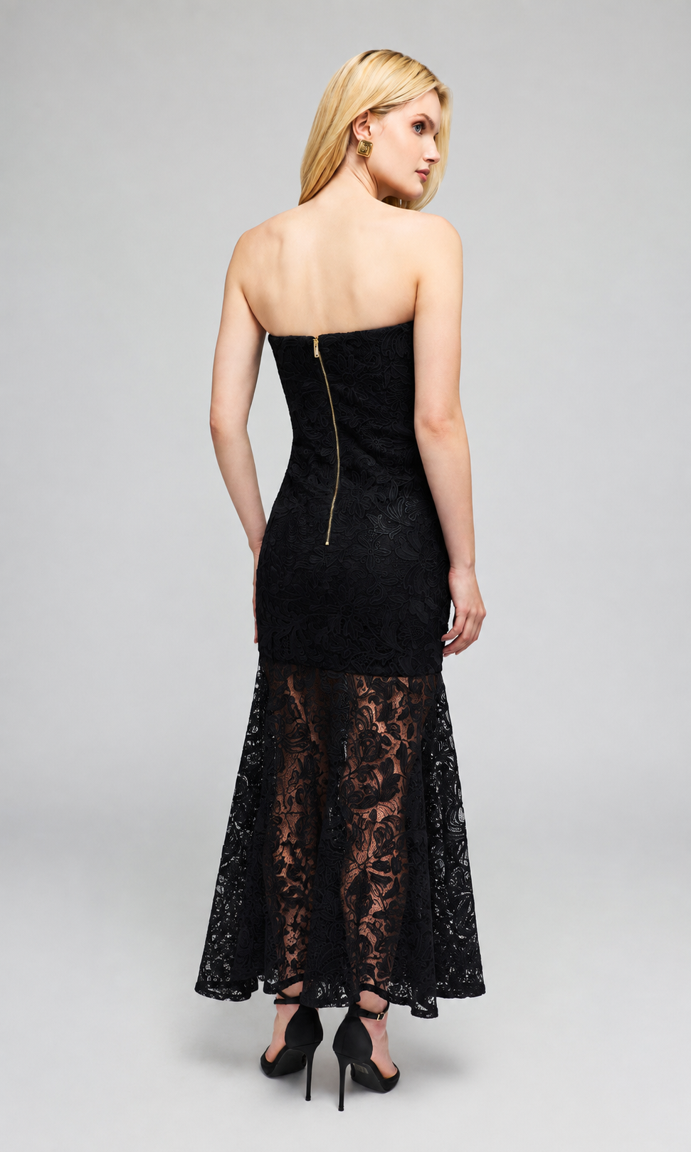 Back view of model wearing a strapless black lace maxi dress from the back, showing a gold zipper at the back of the bodice.