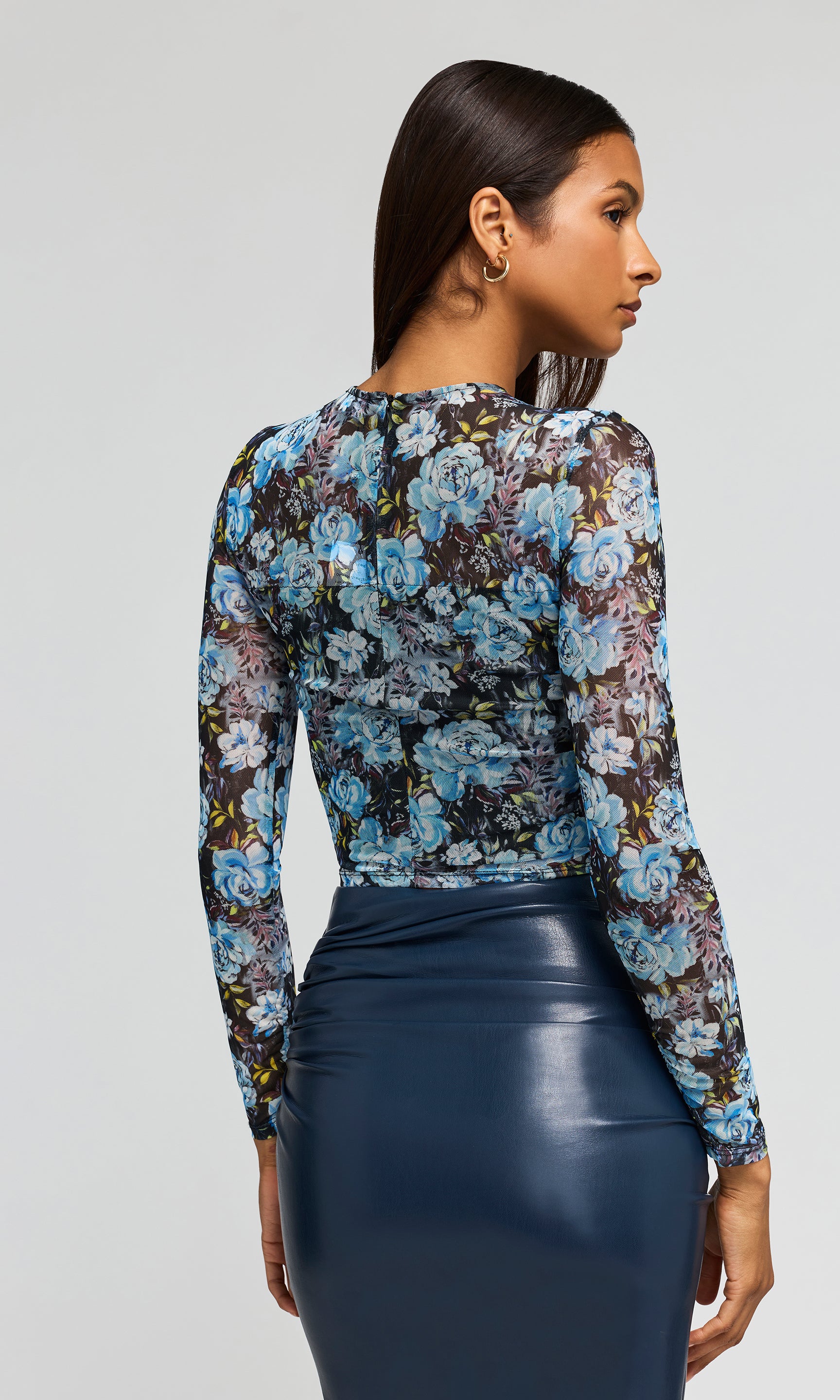 Back view of model wearing a blue floral mesh crop top with a navy vegan leather skirt on a plain background.