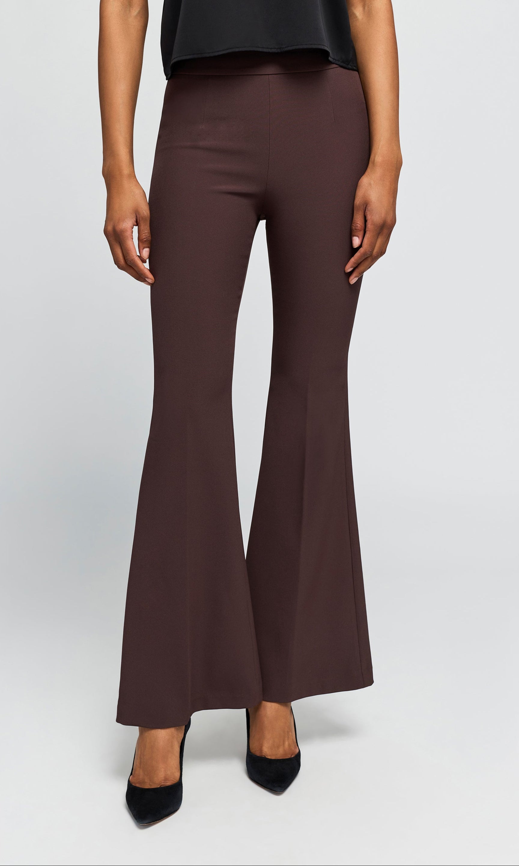 Model wearing a pair of dark brown flared pants with black pointed-toe heels, on a plain background.