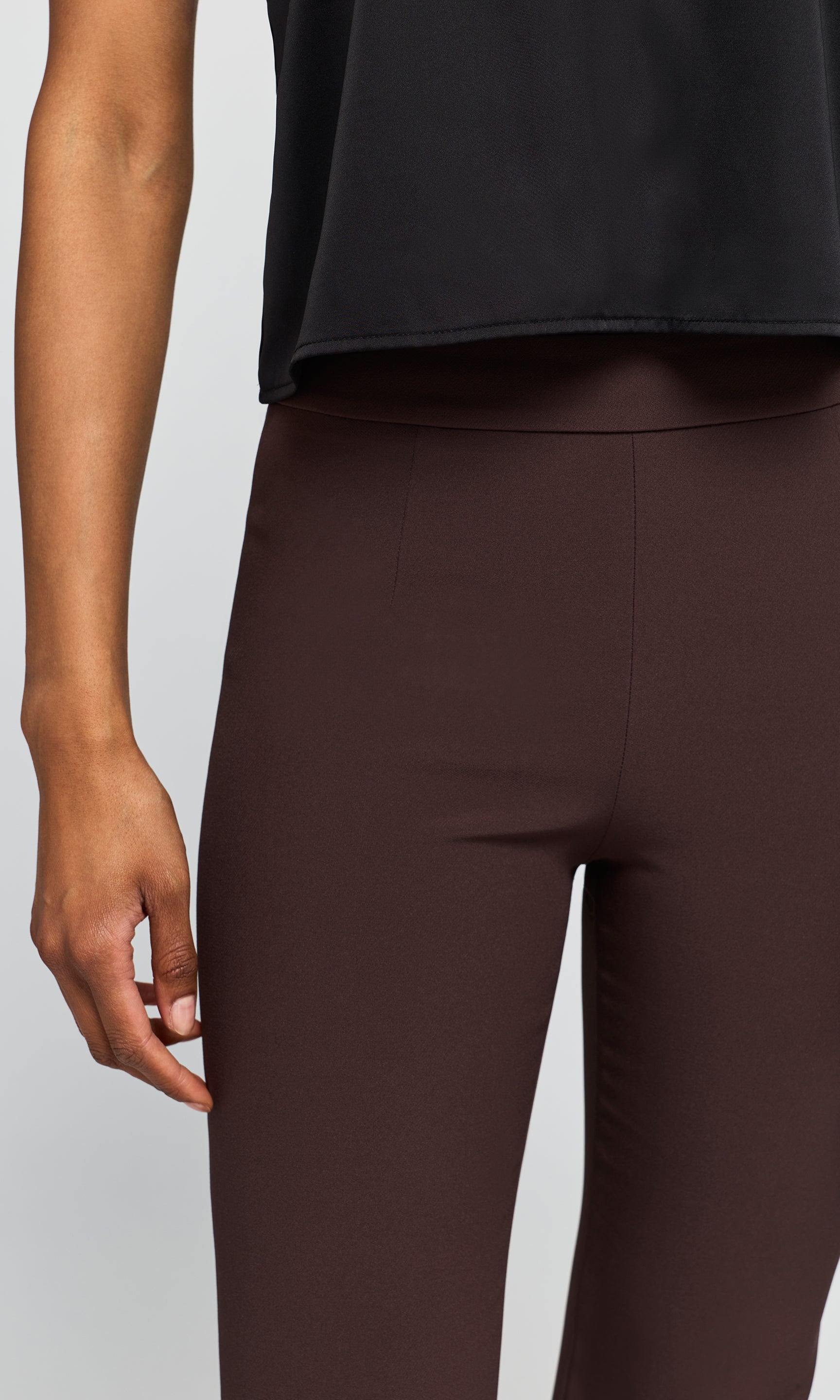 Close-up of a model wearing dark brown trouser and a black cropped top against a light gray studio background.