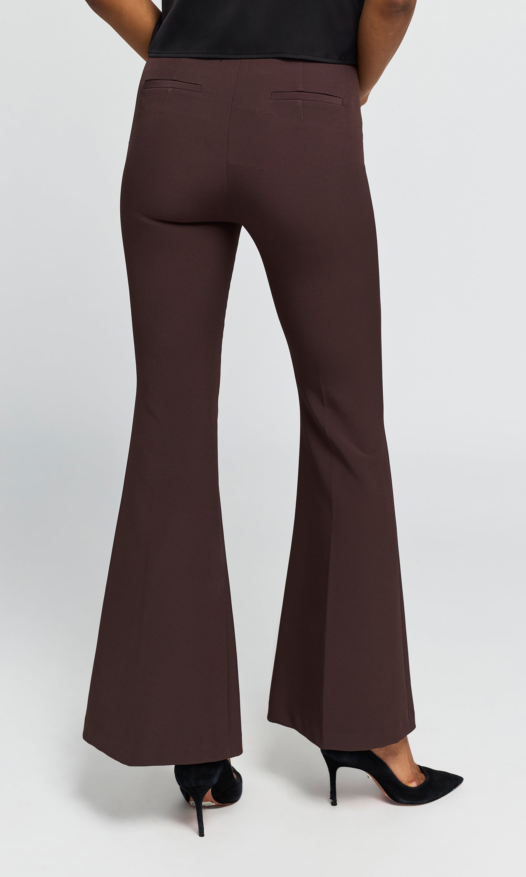 Back view of model wearing brown crepe flared trousers with a black top on a plain background.