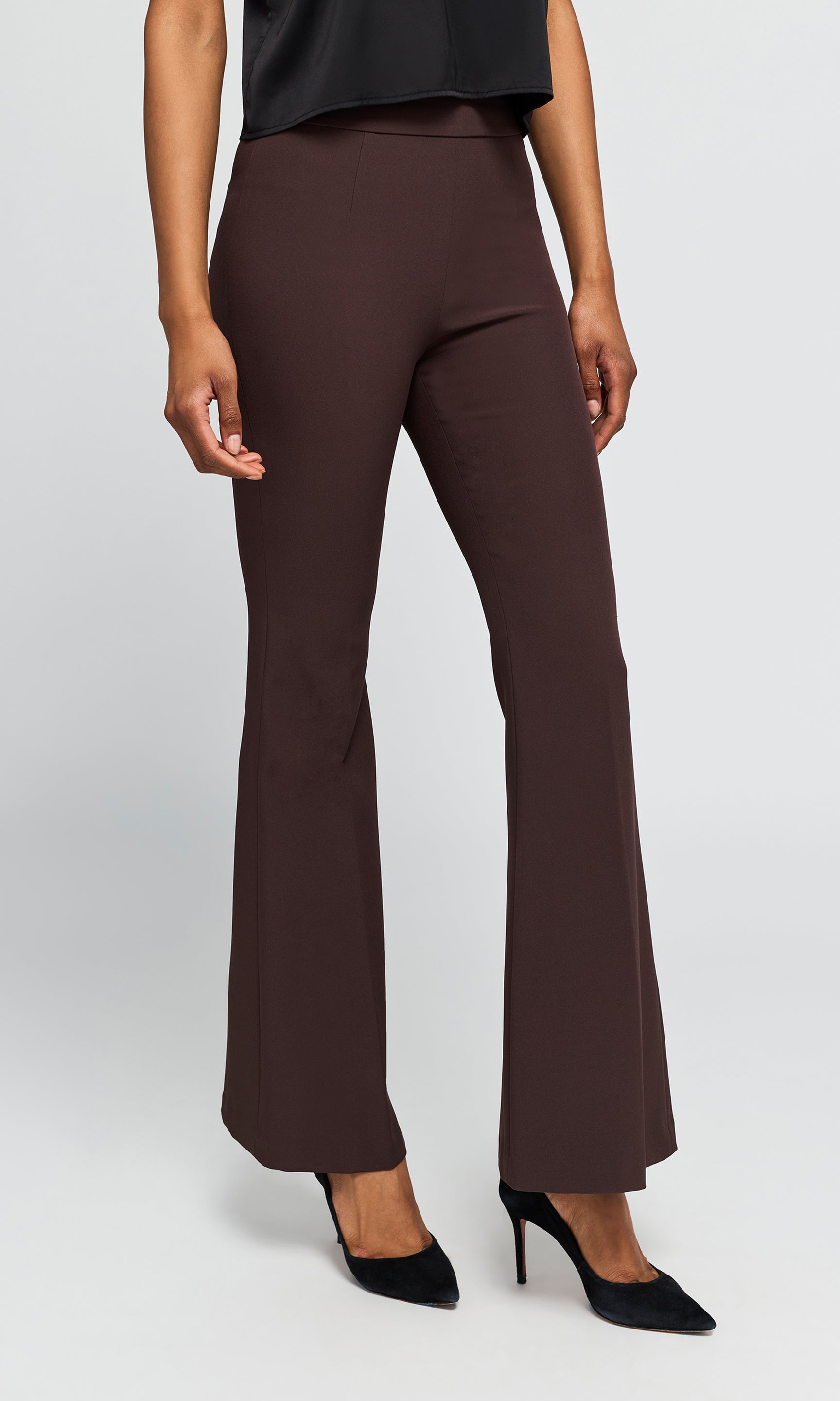 Side view of model wearing brown crepe flared trousers with a black top on a plain background.