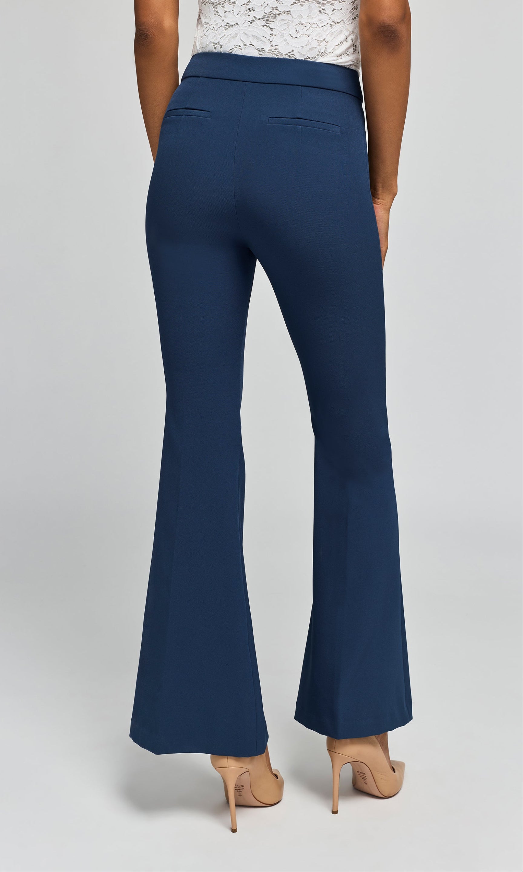 Back view of model wearing navy crepe pants with a white top and beige heels on a plain background.