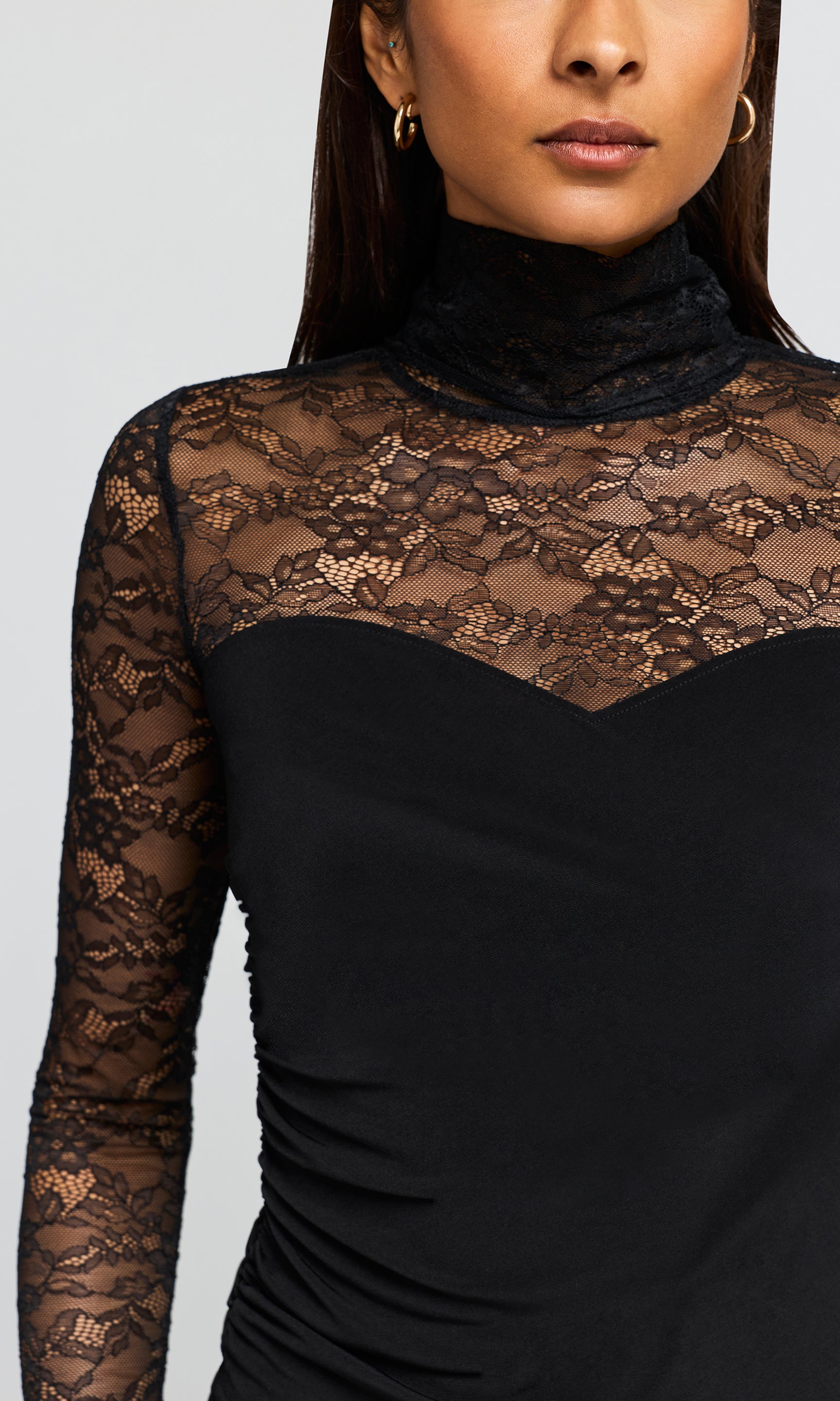 A close-up of a black mock neck top with sheer floral lace sleeves and a sheer lace yoke across the chest.