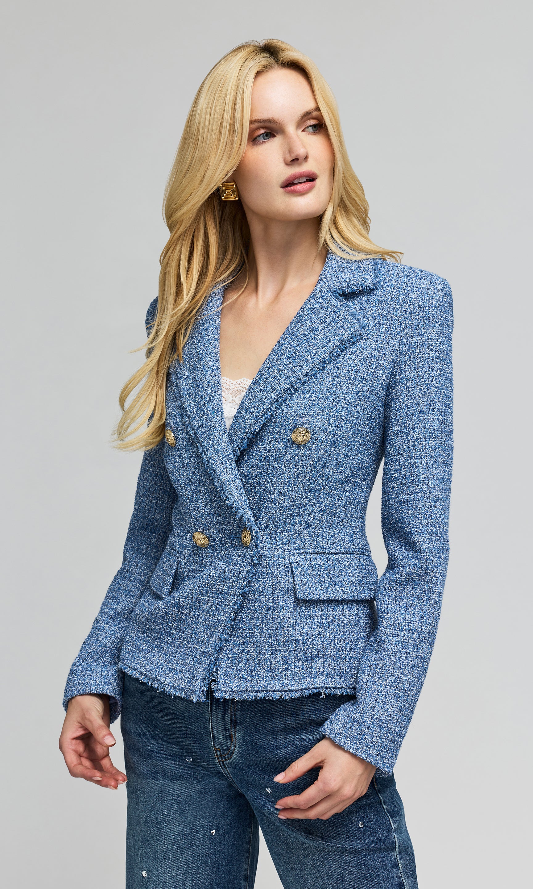 Side view of model wears a tweed blue double-breasted blazer with gold buttons, paired with blue jeans, against plain background.