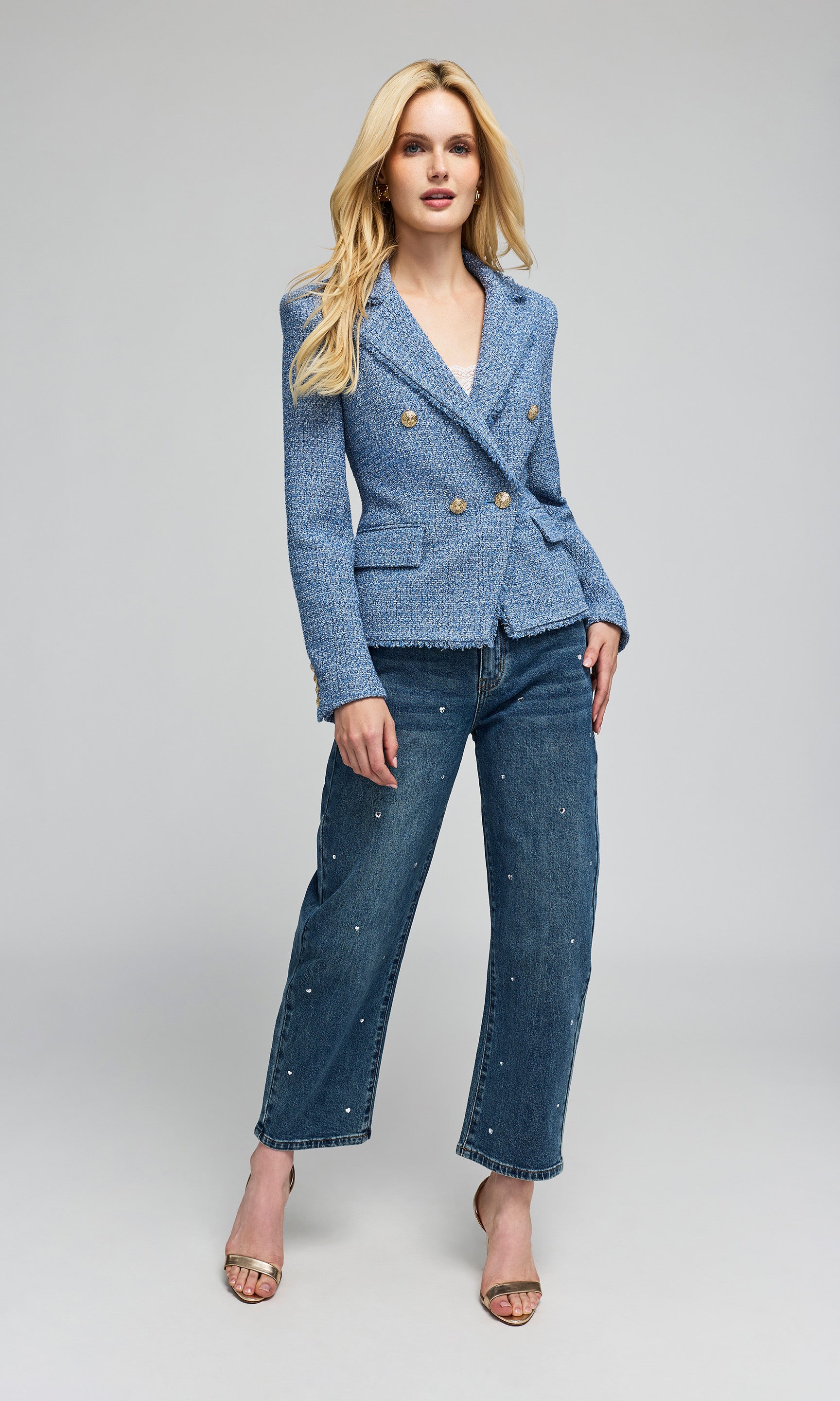 Model wearing a tweed blue double-breasted blazer with gold buttons and blue jeans with crystal embellishments.