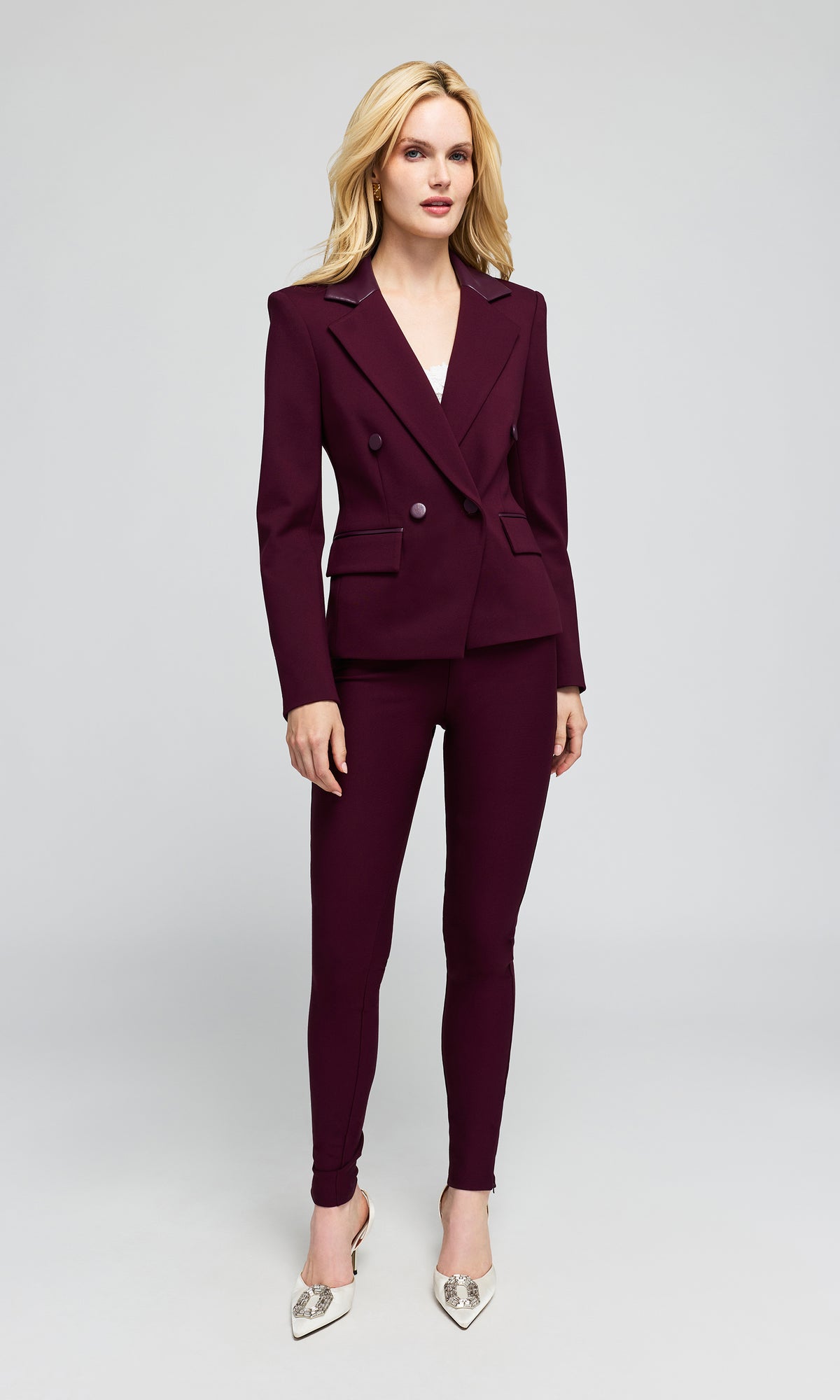 Model wearing a matching deep burgundy double-breasted blazer and slim-fit trousers set, paired with white pointed-toe heels.