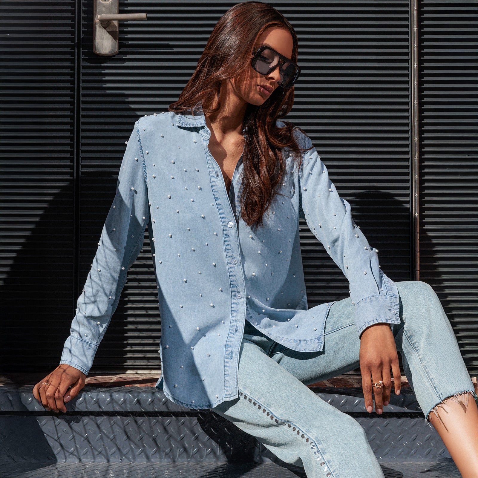 Woman wearing a light blue denim outfit sitting against a dark textured wall.