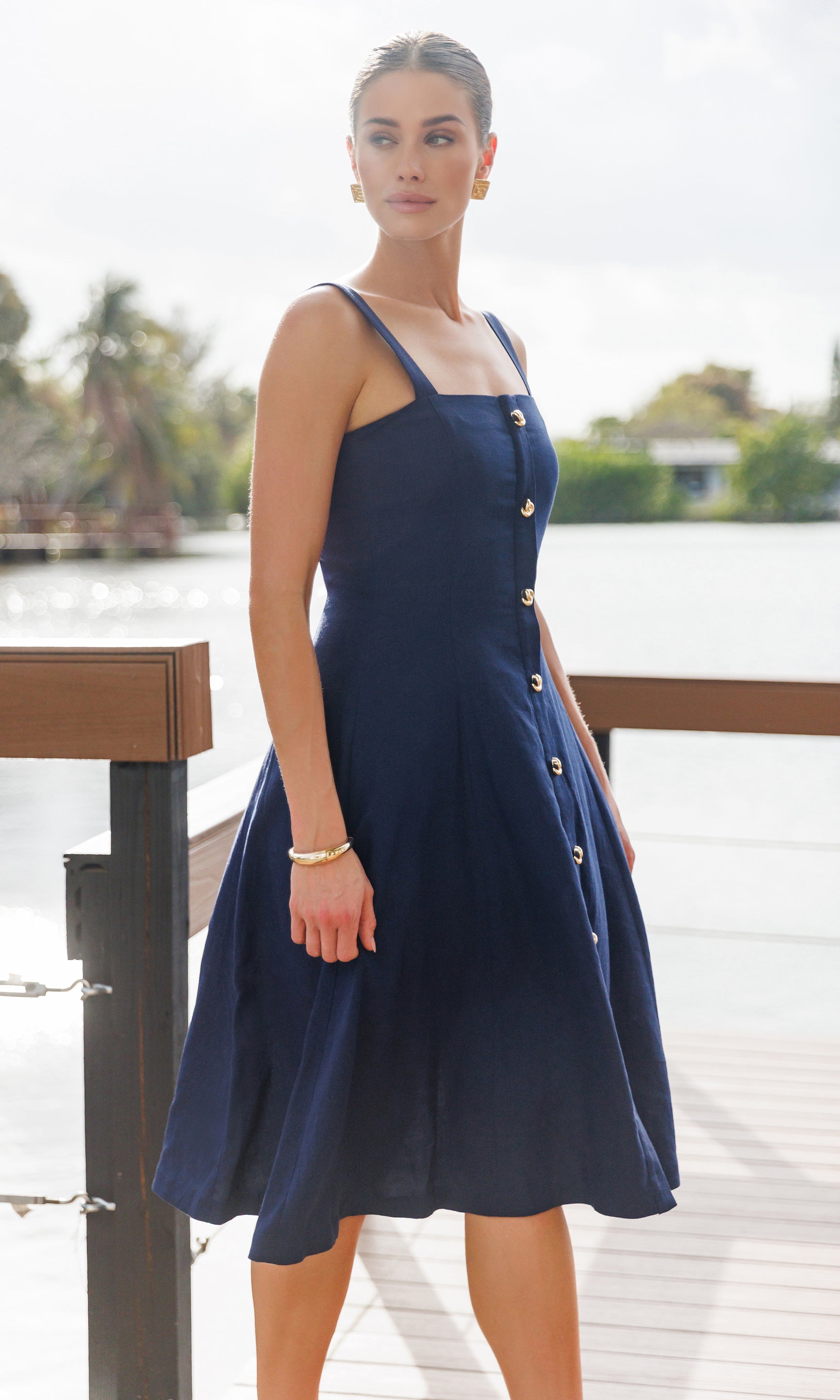 Woman wearing a navy blue dress with buttons by a waterfront