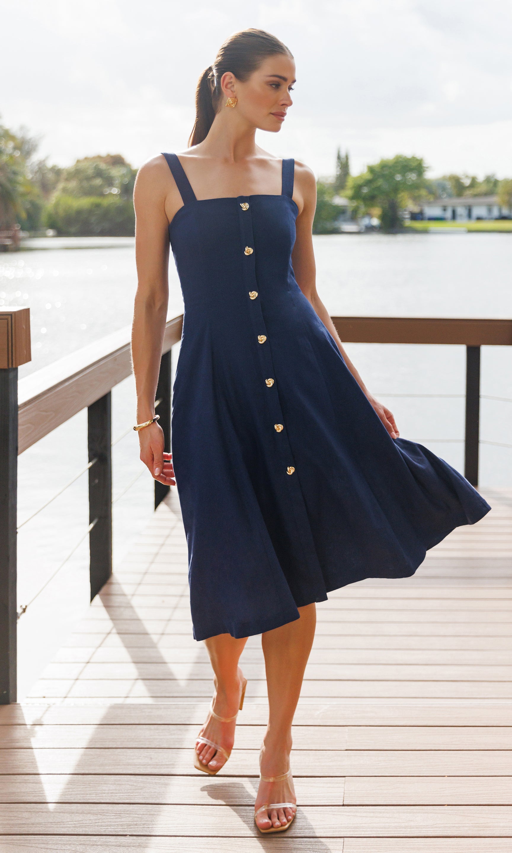 Woman wearing a navy blue dress with gold buttons by a waterfront