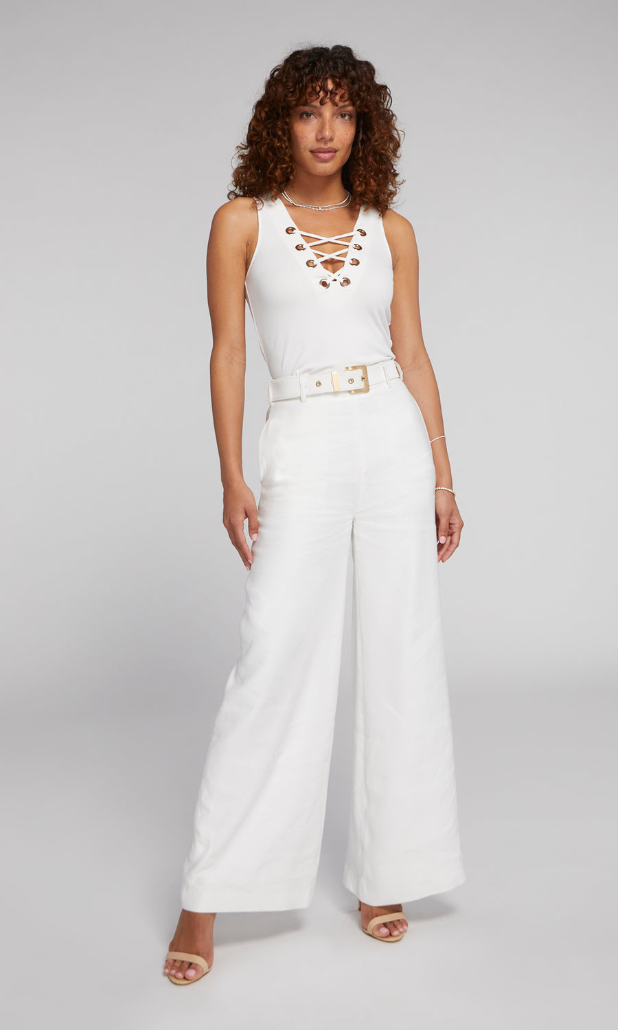 The image features a woman in a fashionable white lace-up top with gold details, highlighting a contemporary and sophisticated look.