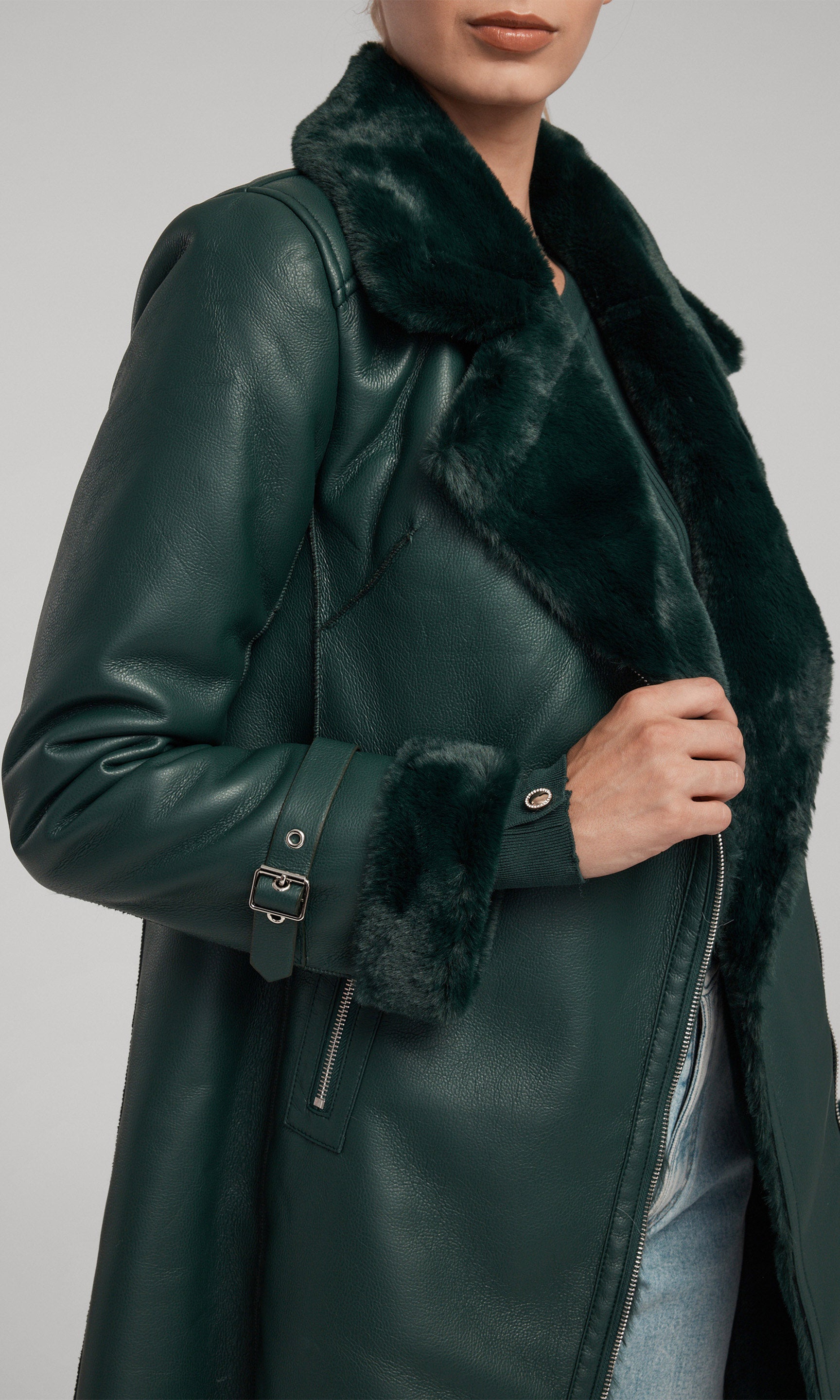 A model showcases a stylish green suede coat adorned with a luxurious faux fur collar, exuding elegance and sophistication.