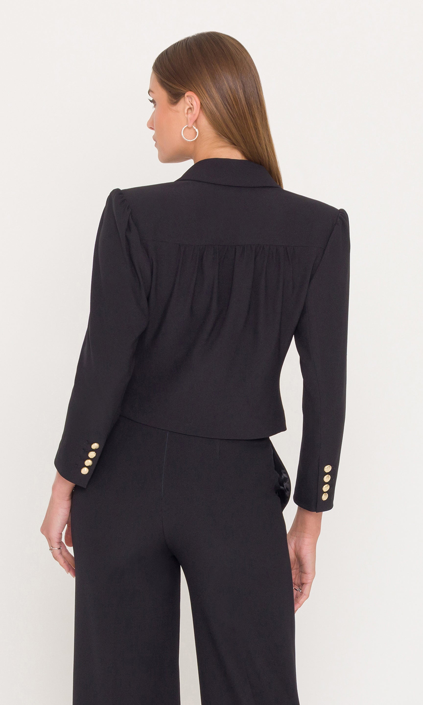 Back view of woman wearing a black outfit with gold buttons on a white background