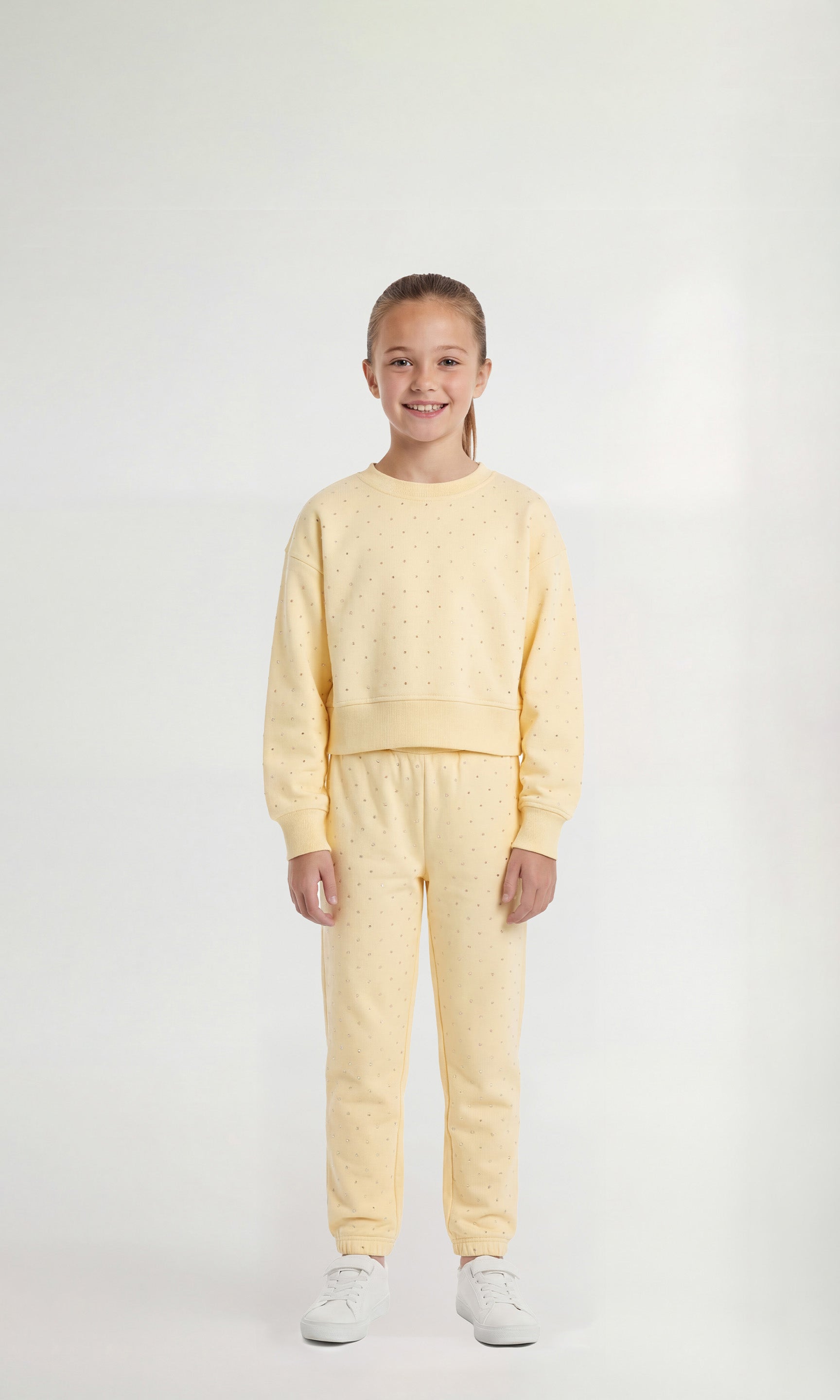 Young girl wearing a light yellow sweatsuit with crystal embellishments on a white background