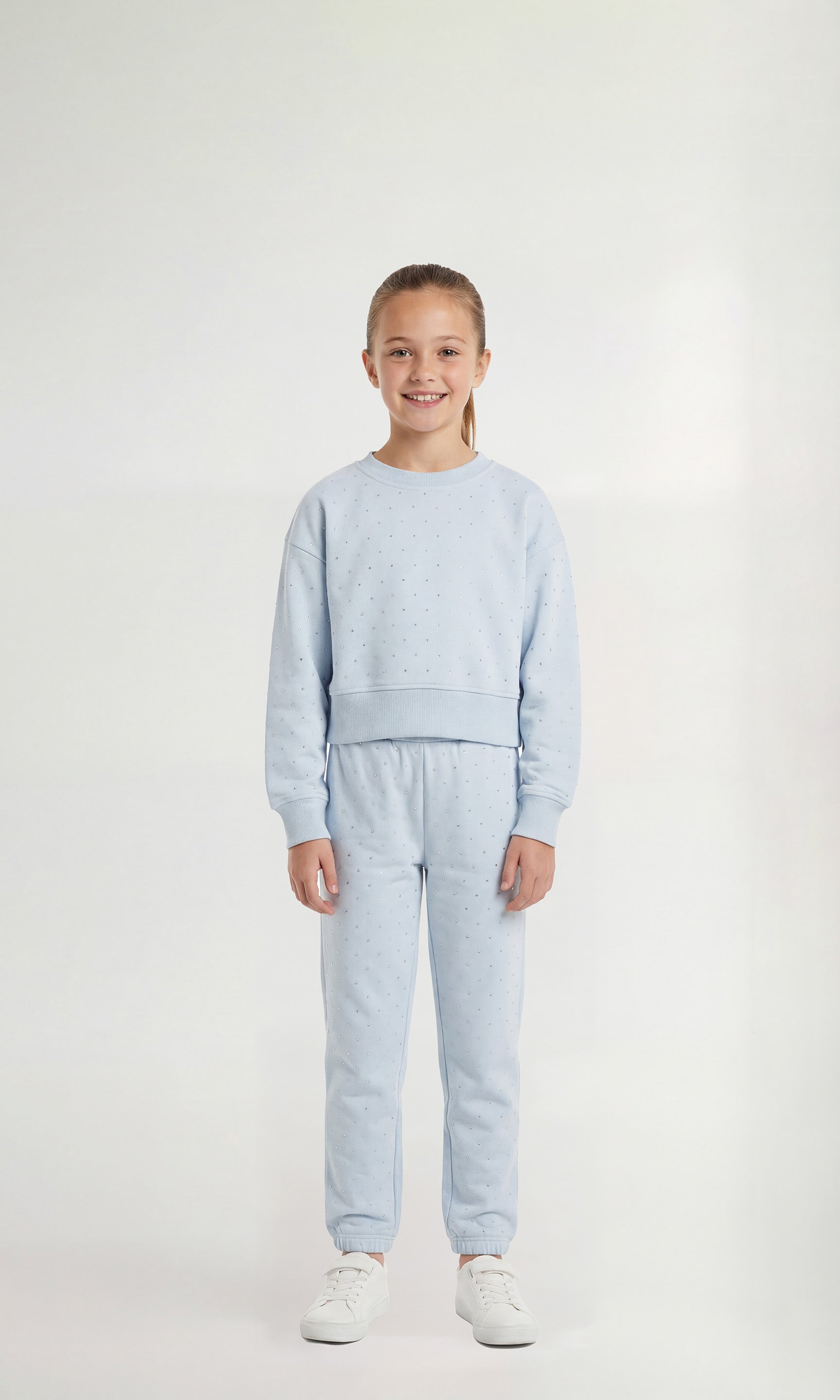 Young girl wearing a light blue sweatsuit with crystal embellishments on a white background