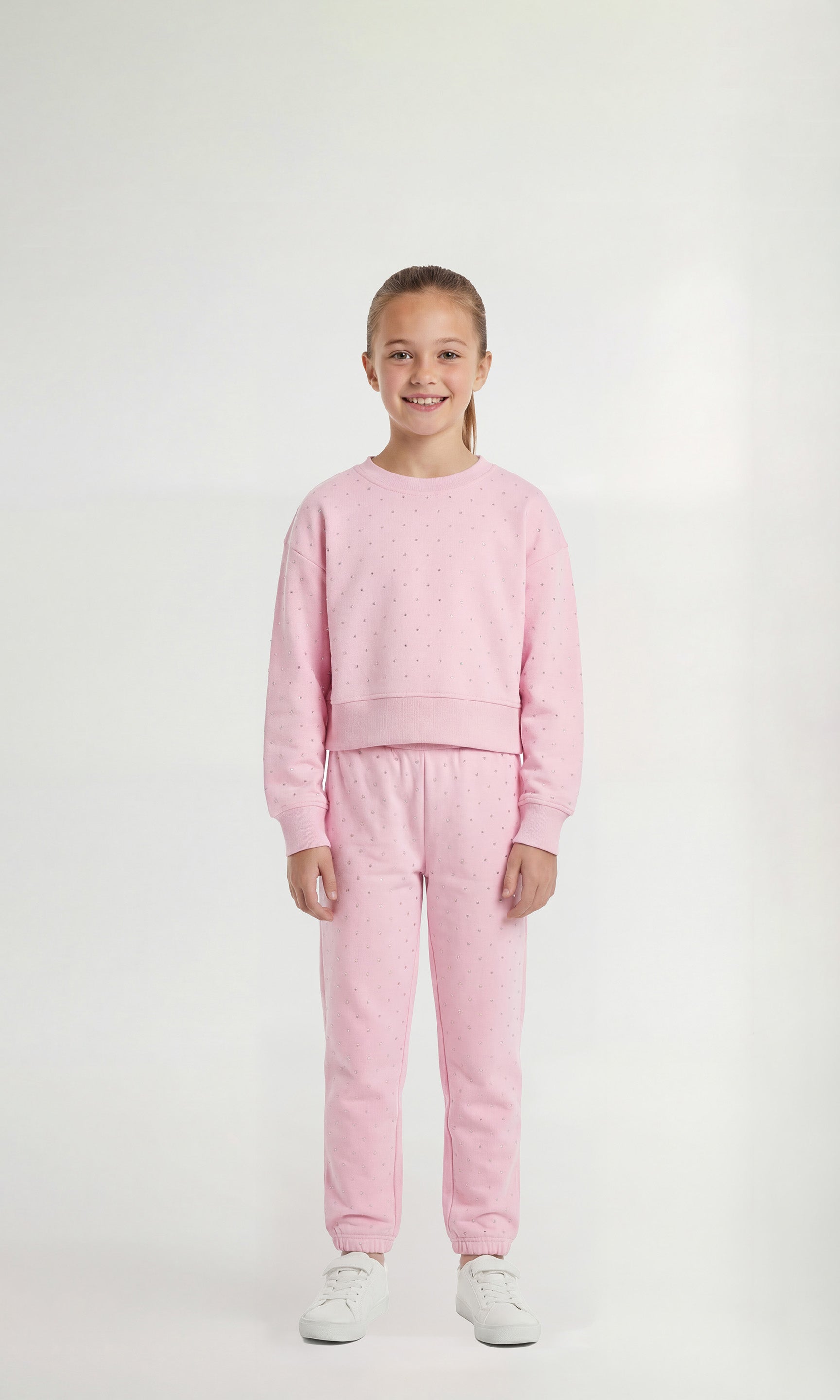 Young girl wearing a pink sweatsuit with crystal embellishments on a white background