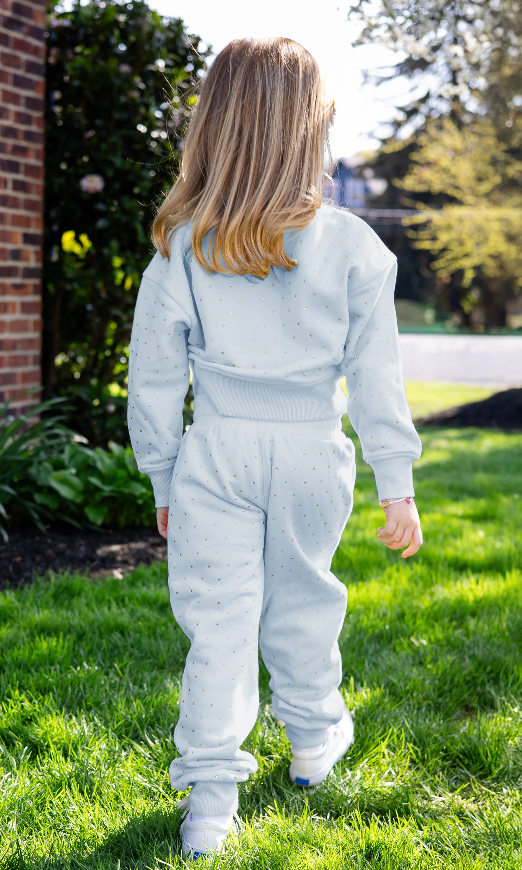 Person wearing a light blue tracksuit standing on grass with a garden background