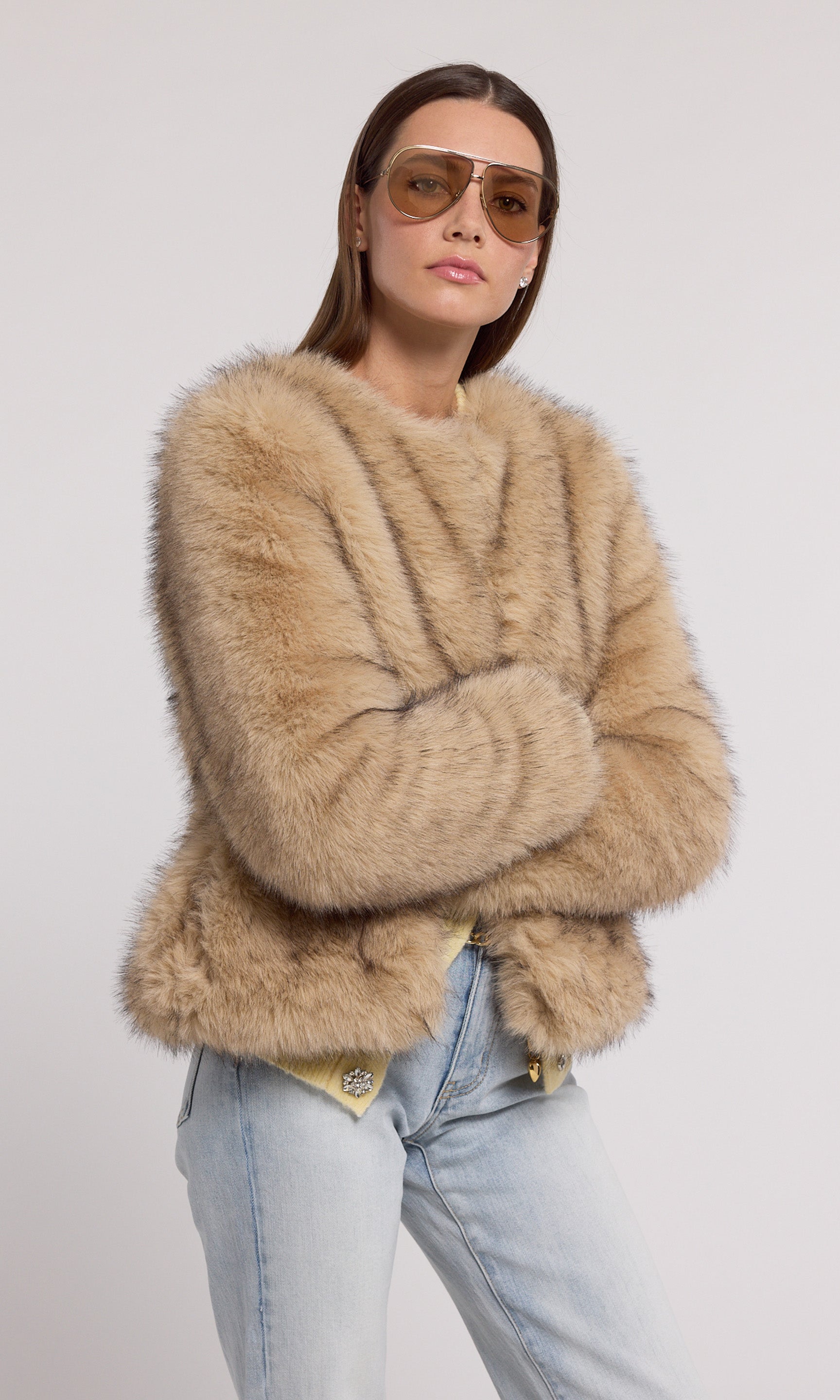 A model showcases a stylish tan faux fur jacket, exuding elegance and warmth in a chic setting.