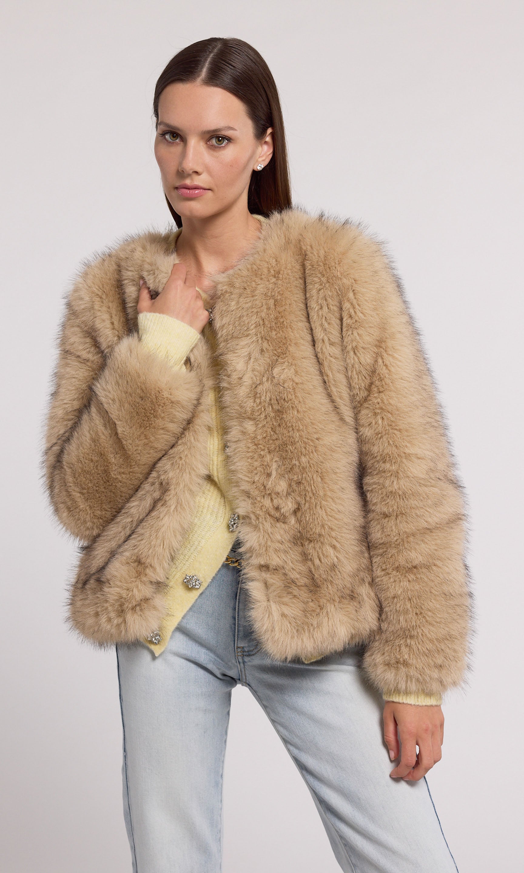 A model showcases a stylish tan faux fur jacket, exuding elegance and warmth in a chic setting.