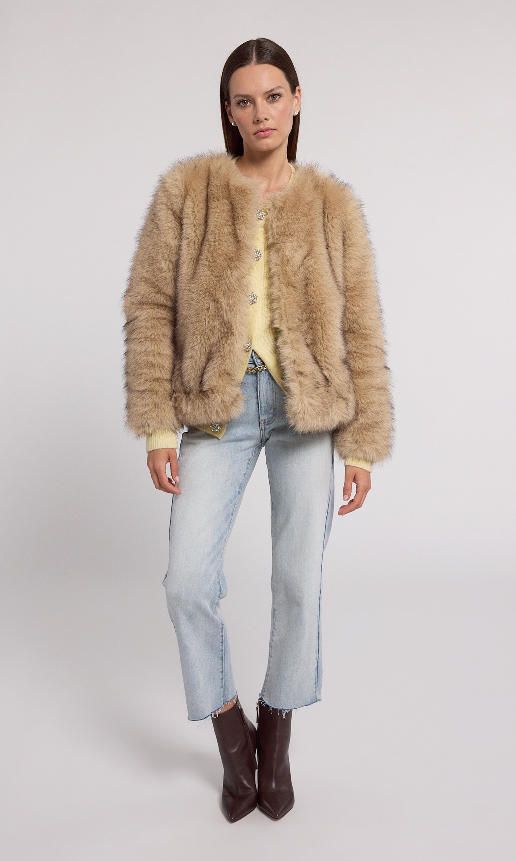 A model showcases a stylish tan faux fur jacket, exuding elegance and warmth in a chic setting.