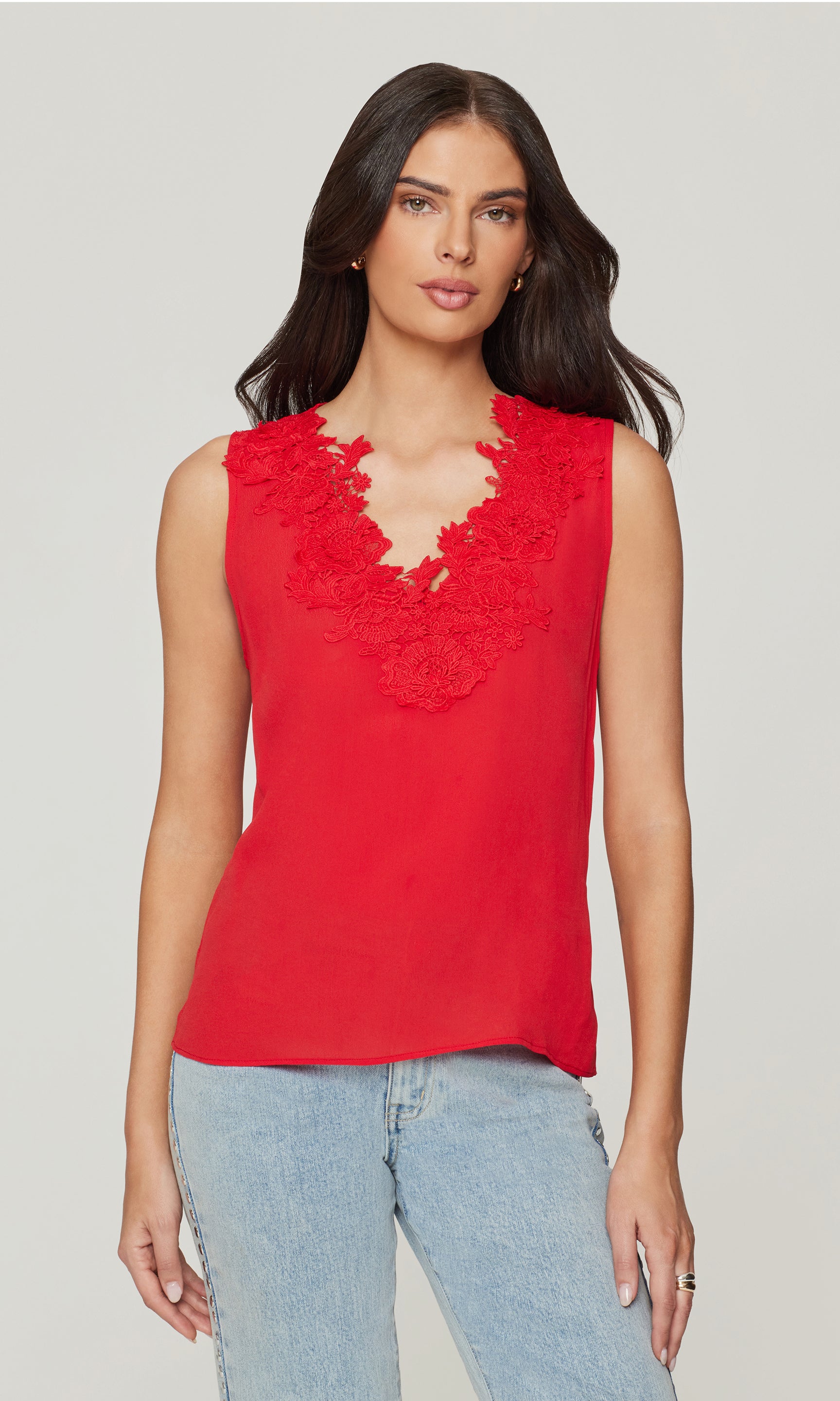 Woman wearing a red sleeveless top with lace details on a plain background