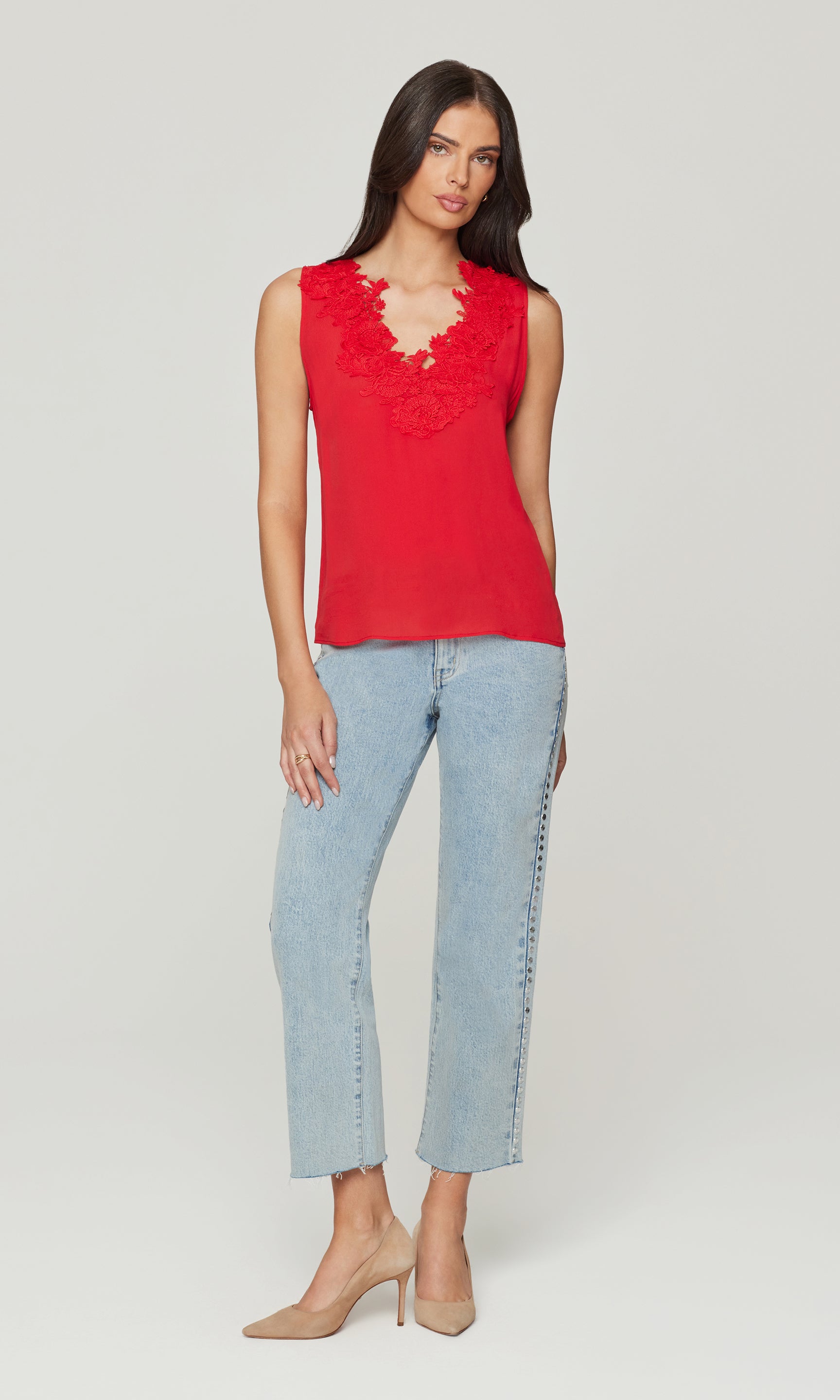 Woman wearing a red sleeveless top with lace details and light blue jeans on a white background
