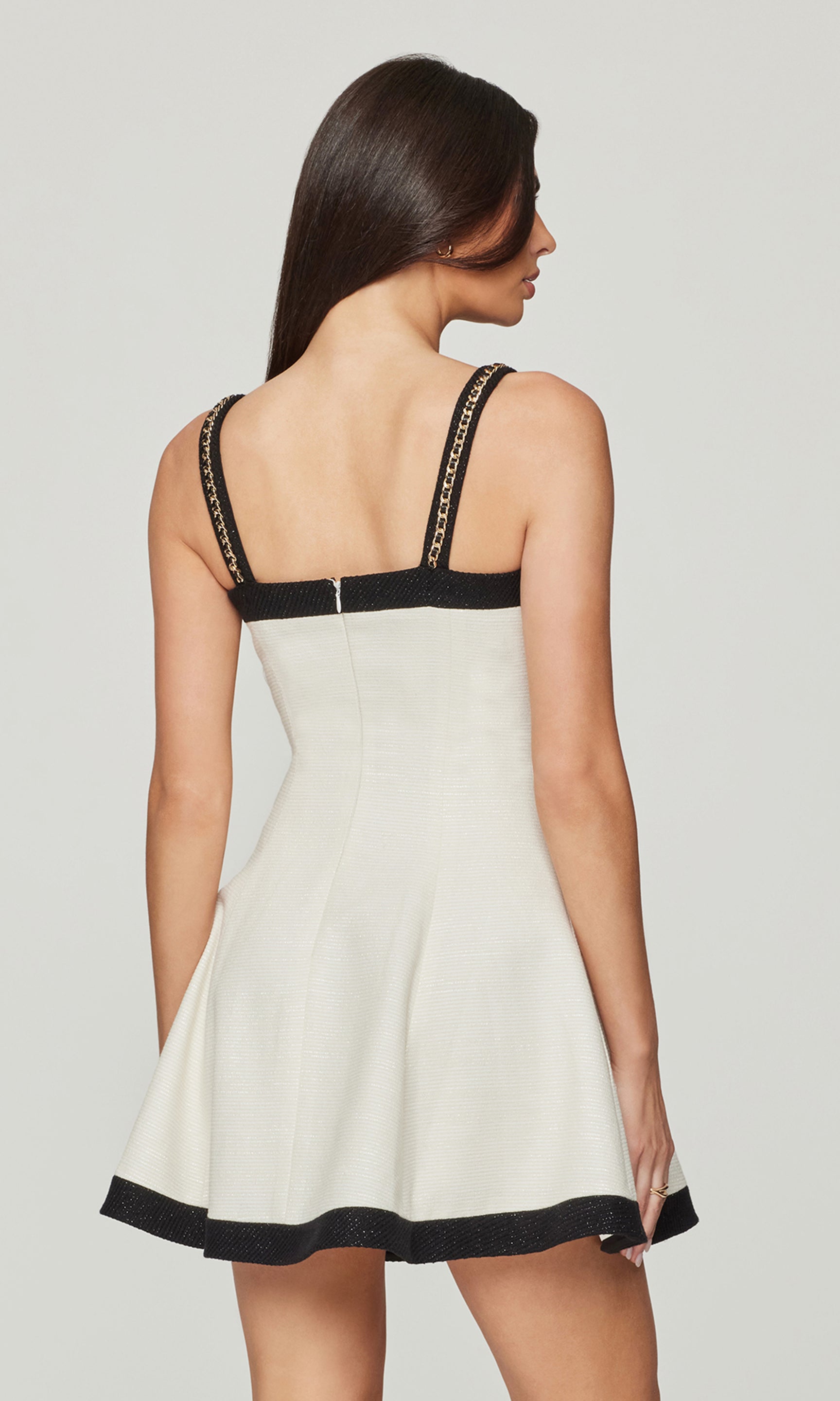 Back view of woman wearing a white dress with black trim on a plain background