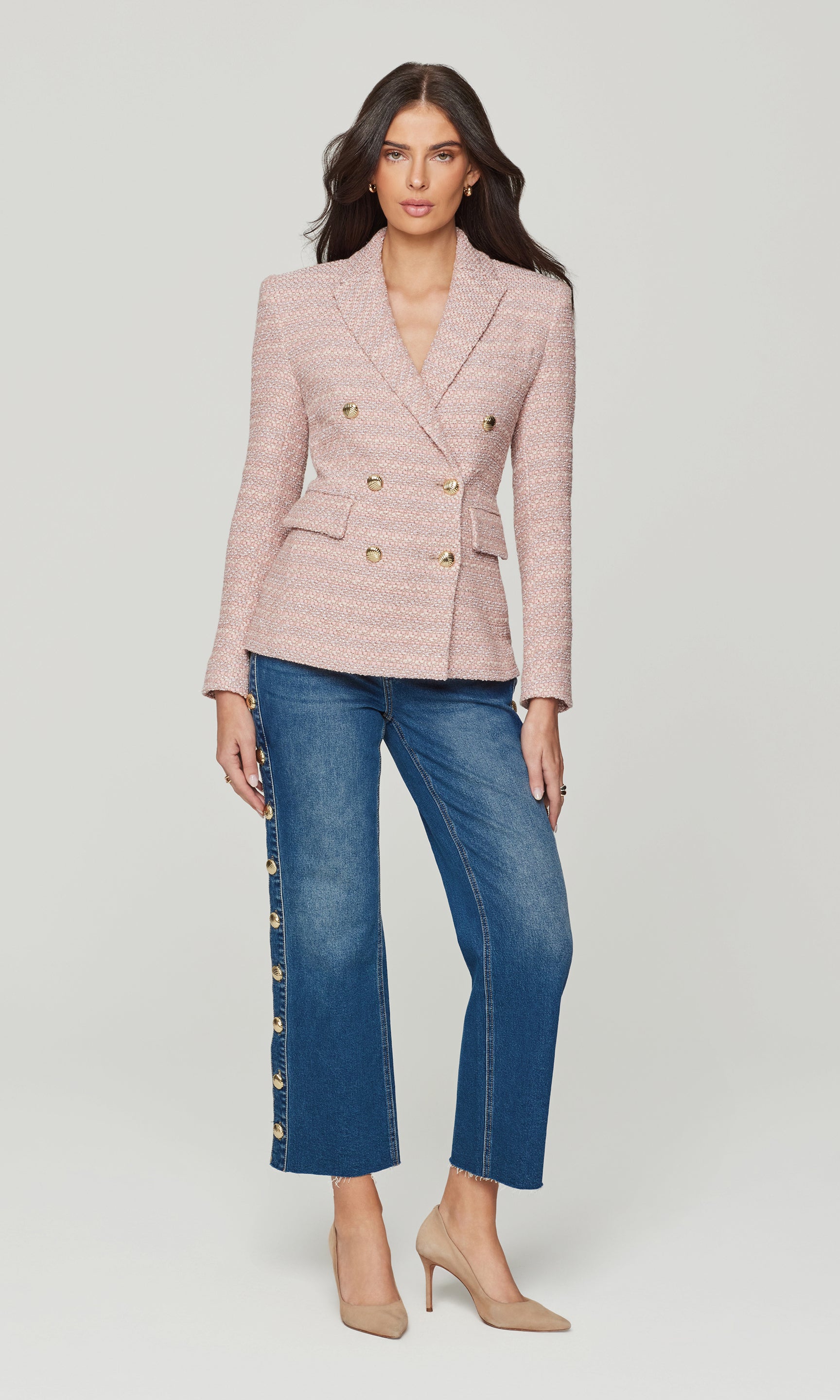 Full body image of woman wearing a pink tweed blazer and blue jeans with gold buttons on a white background