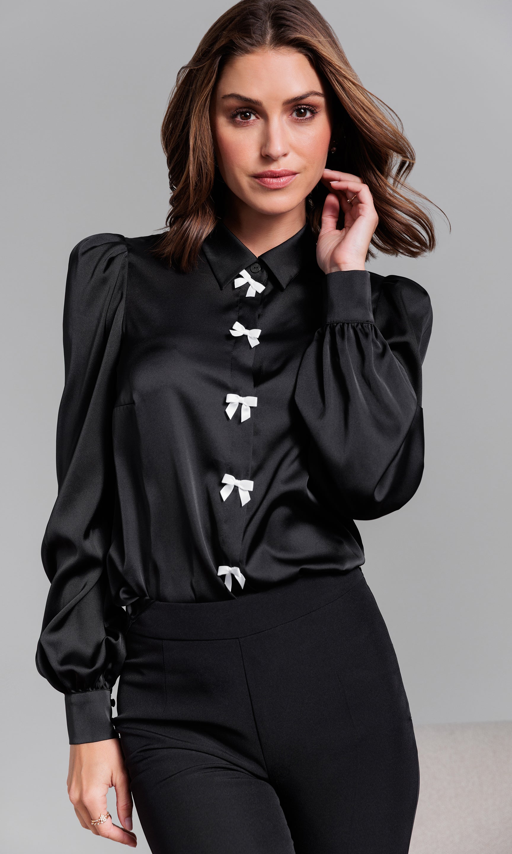 Woman wearing a black blouse with white bow details on a gray background