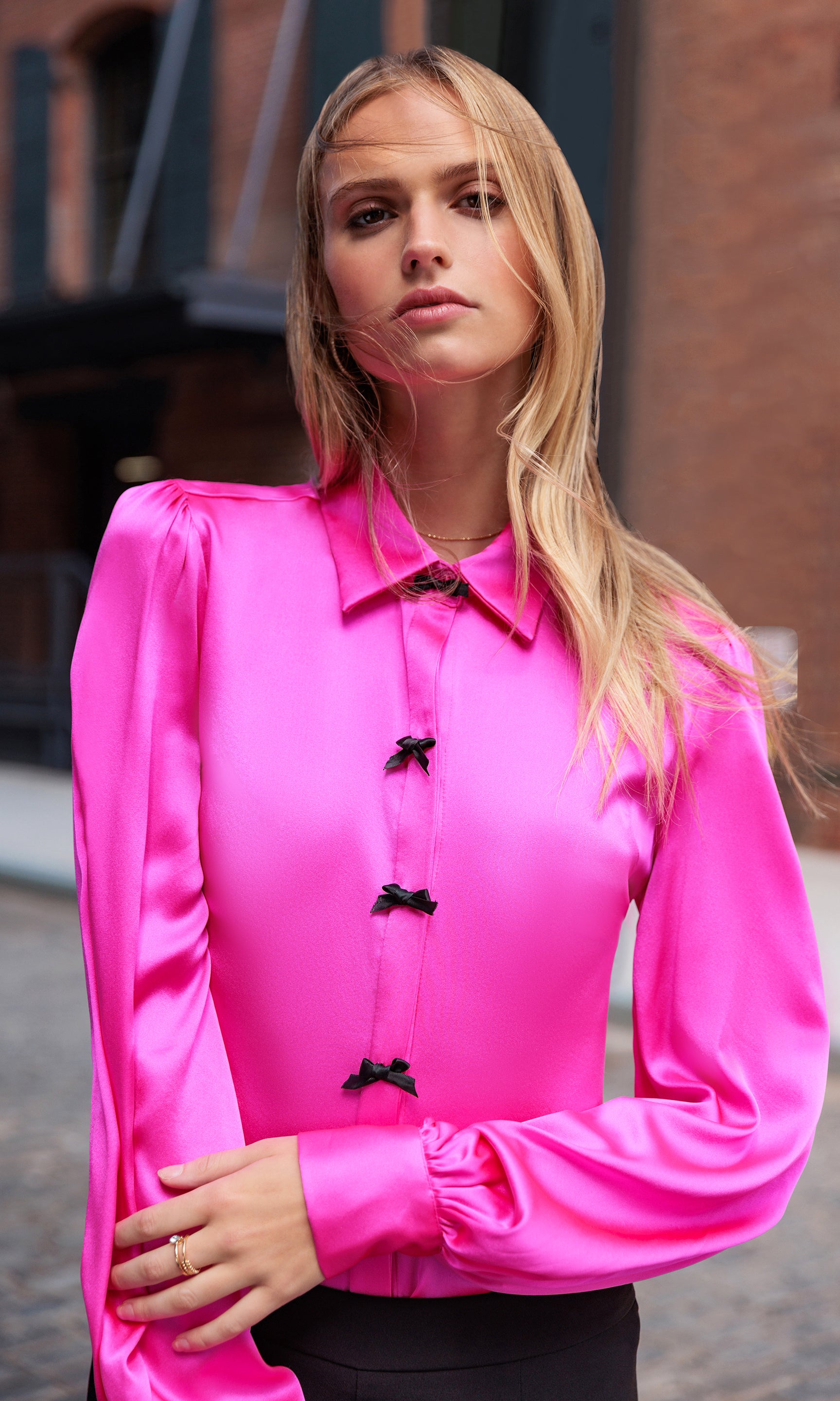 Woman wearing a bright pink blouse with black bow buttons outdoors.