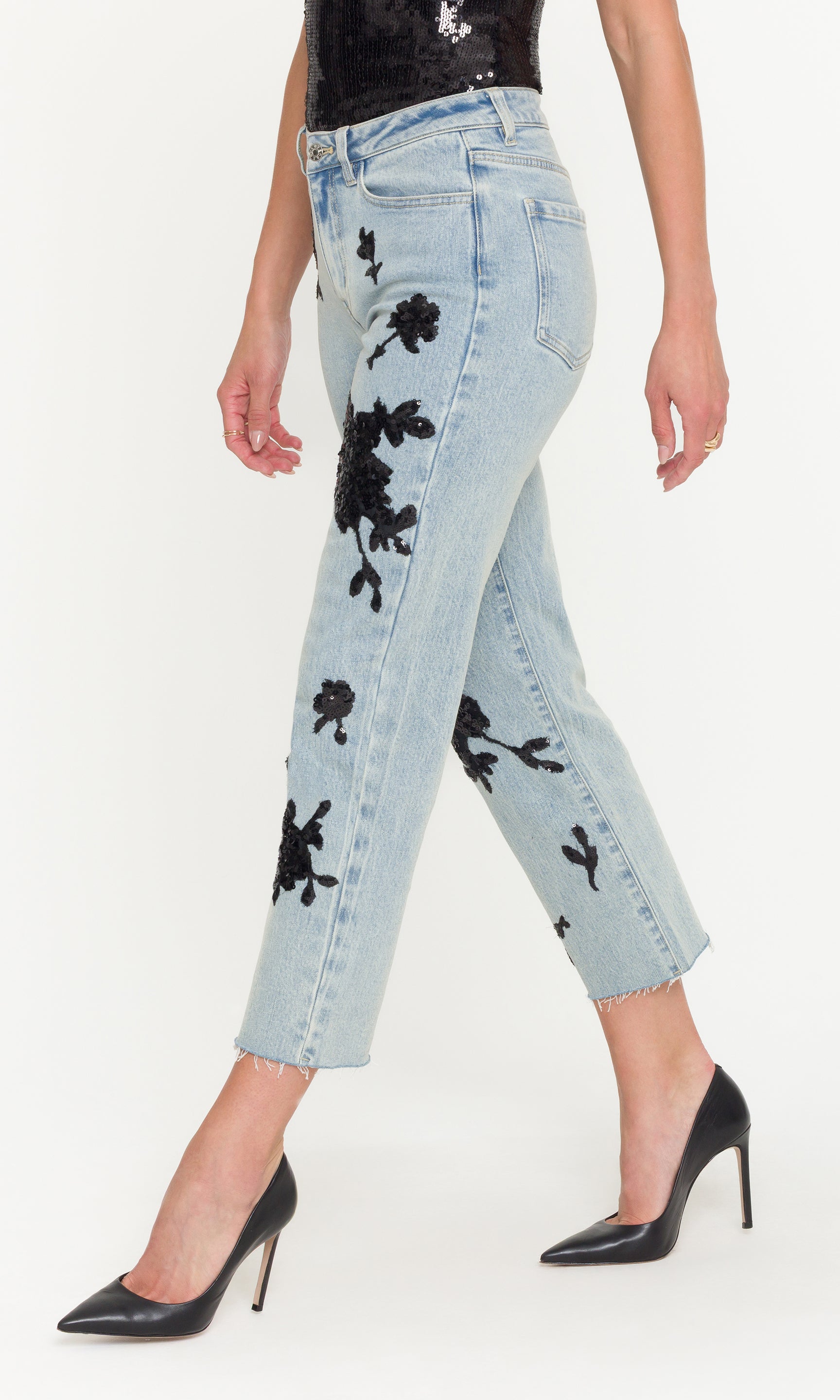 Side view of light blue jeans with black floral sequin patterns worn by a person on a white background